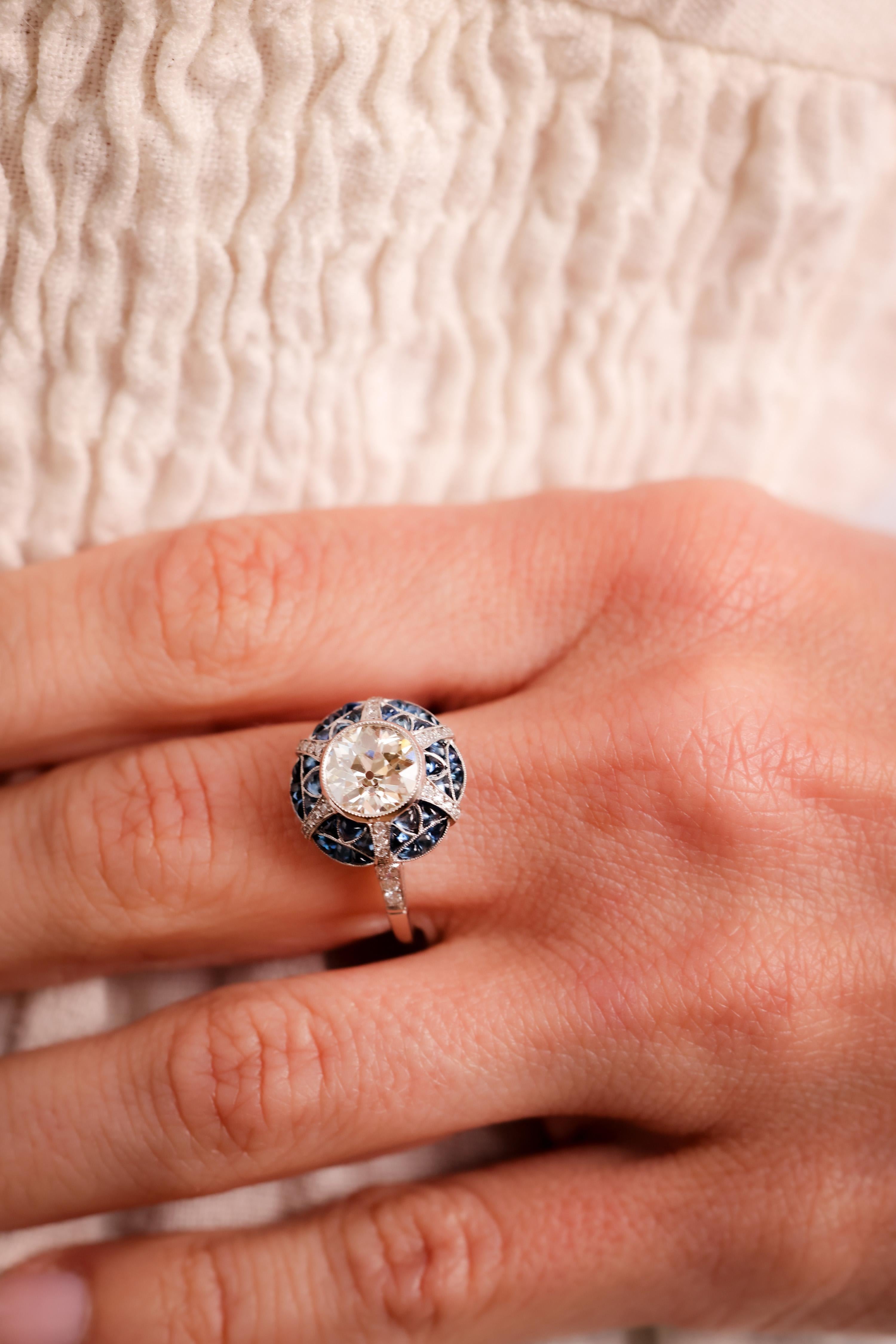 Center Stone: Diamond
Cut: Old European Cut
Weight: 1.46 Carat
Color: L
Clarity: VS
Accent Stone: 36 Sapphires
Cut: Cabochon Cuts
Weight: Approximately 2.5 Carats
Color: Blue
Accent Stone: 30 Diamonds
Cut: Round Brilliant
Weight: Approximately 0.3