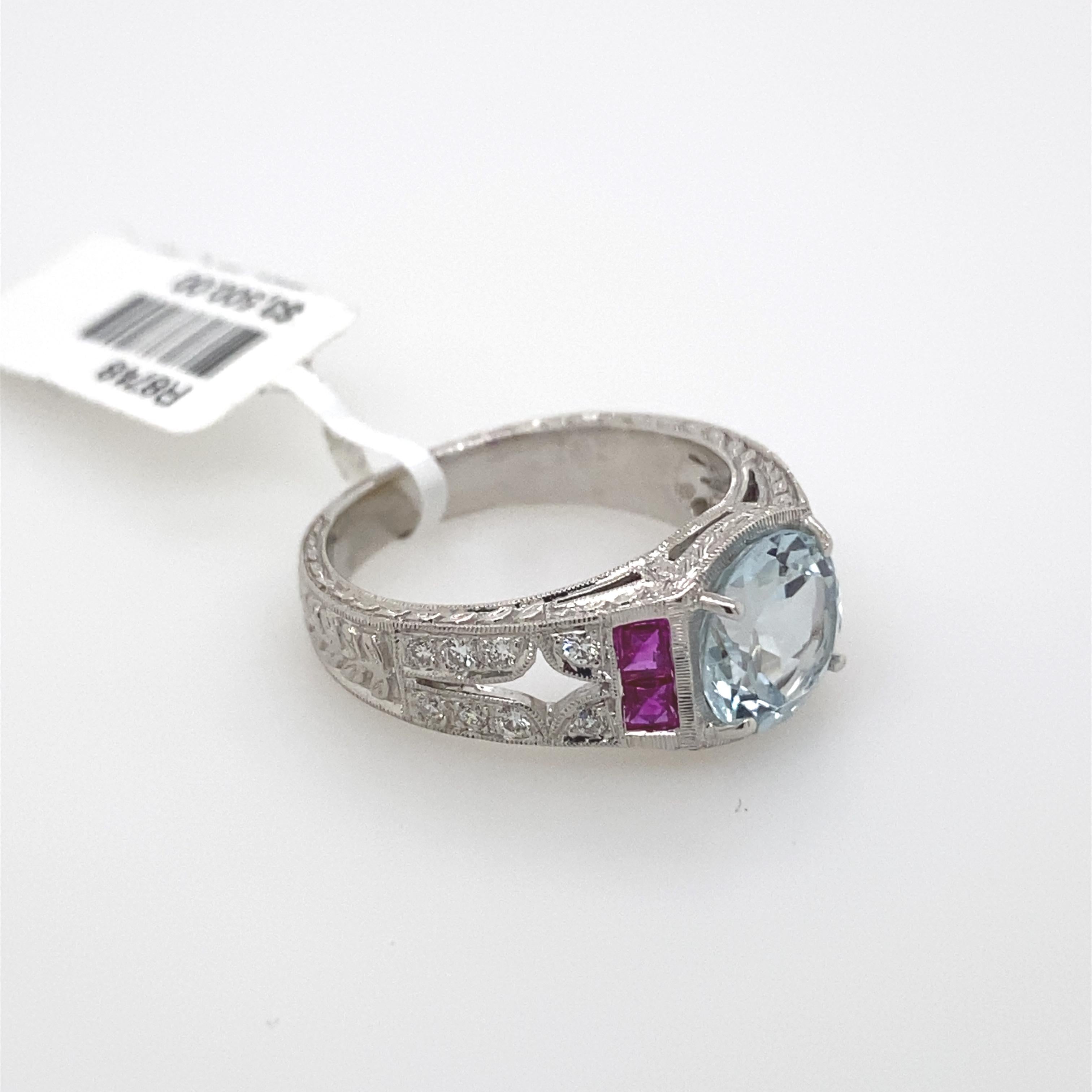 Art Deco inspired ring aquamarine ring. 
2.00ct center round cut aquamarine. Complimented with 0.83ct of French cut rubies and 0.16ct of round cut diamonds. 2.99ct total gemstone weight. 18k white gold with milgrain and filigree work.
Accommodated