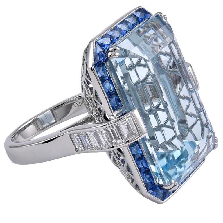 Art Deco inspired ring set in platinum that features a 27.08 carat aquamarine emerald cut center surrounded by French cut blue sapphires with the total weight of 1.84 carats and diamonds with a total weight of 0.74 carats.