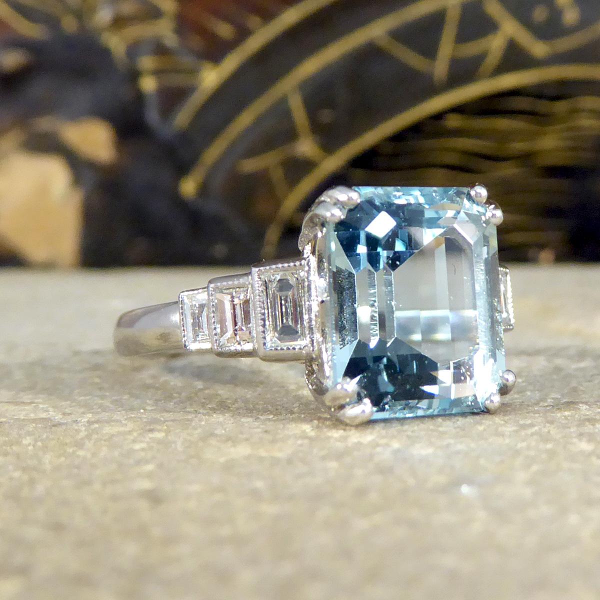 Featuring in this gorgeous ring is a gorgeous and light blue 3.30ct Emerald Cut Aquamarine modelled and designed to resemble a quality popular Art Deco style. On either shoulder sits three Baguette Cut Diamonds graduating in size, from the largest