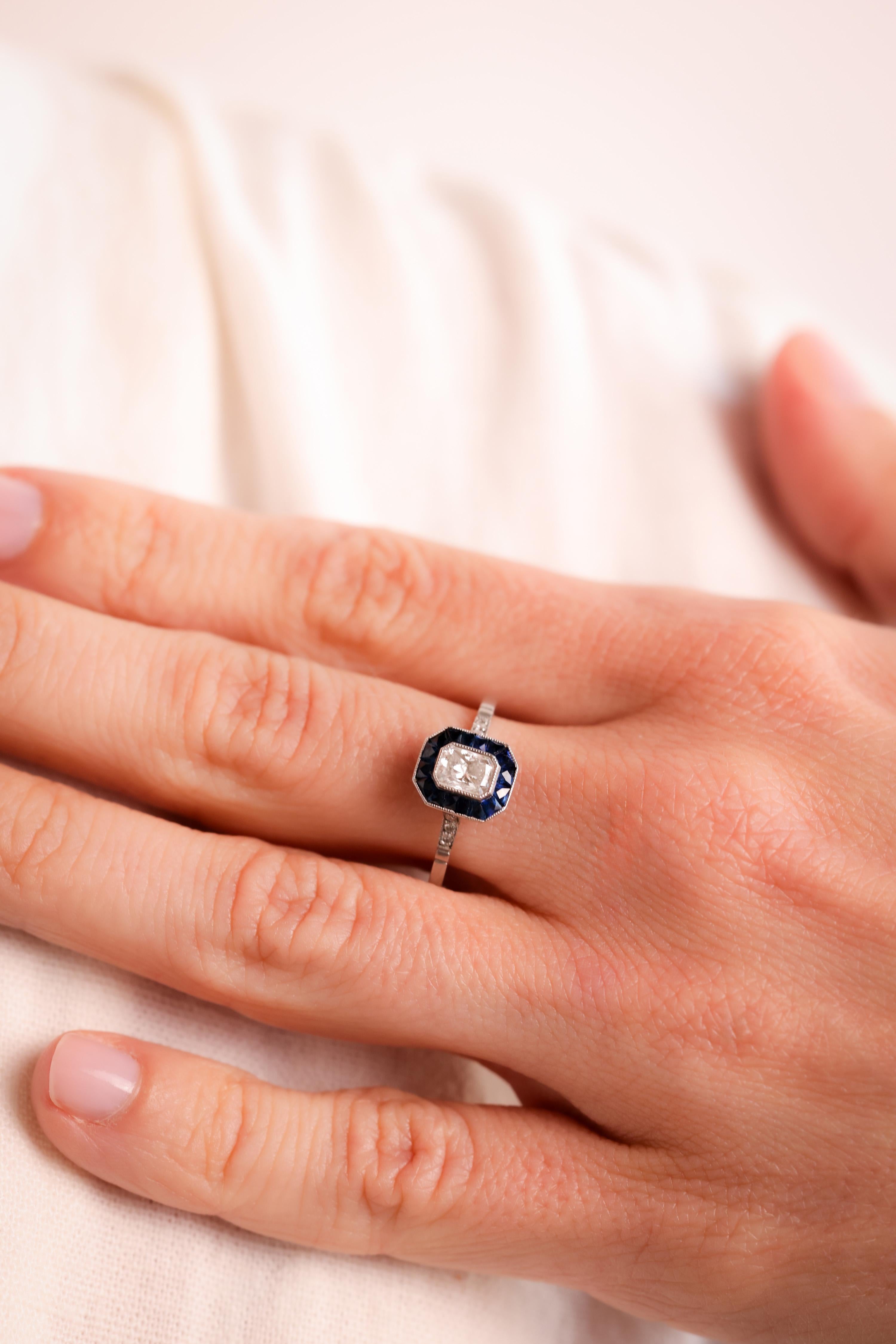 Center Stone: Diamond
Cut: Radiant Cut
Weight: 0.47 Carat
Color: I
Clarity: VS
Accent Stone: 16 Sapphires
Cut: Calibre Cut
Weight: Approximately 0.8 Carats
Color: Blue
Accent Stone: 6 Diamonds
Cut: Round Brilliant
Weight: Approximately 0.06