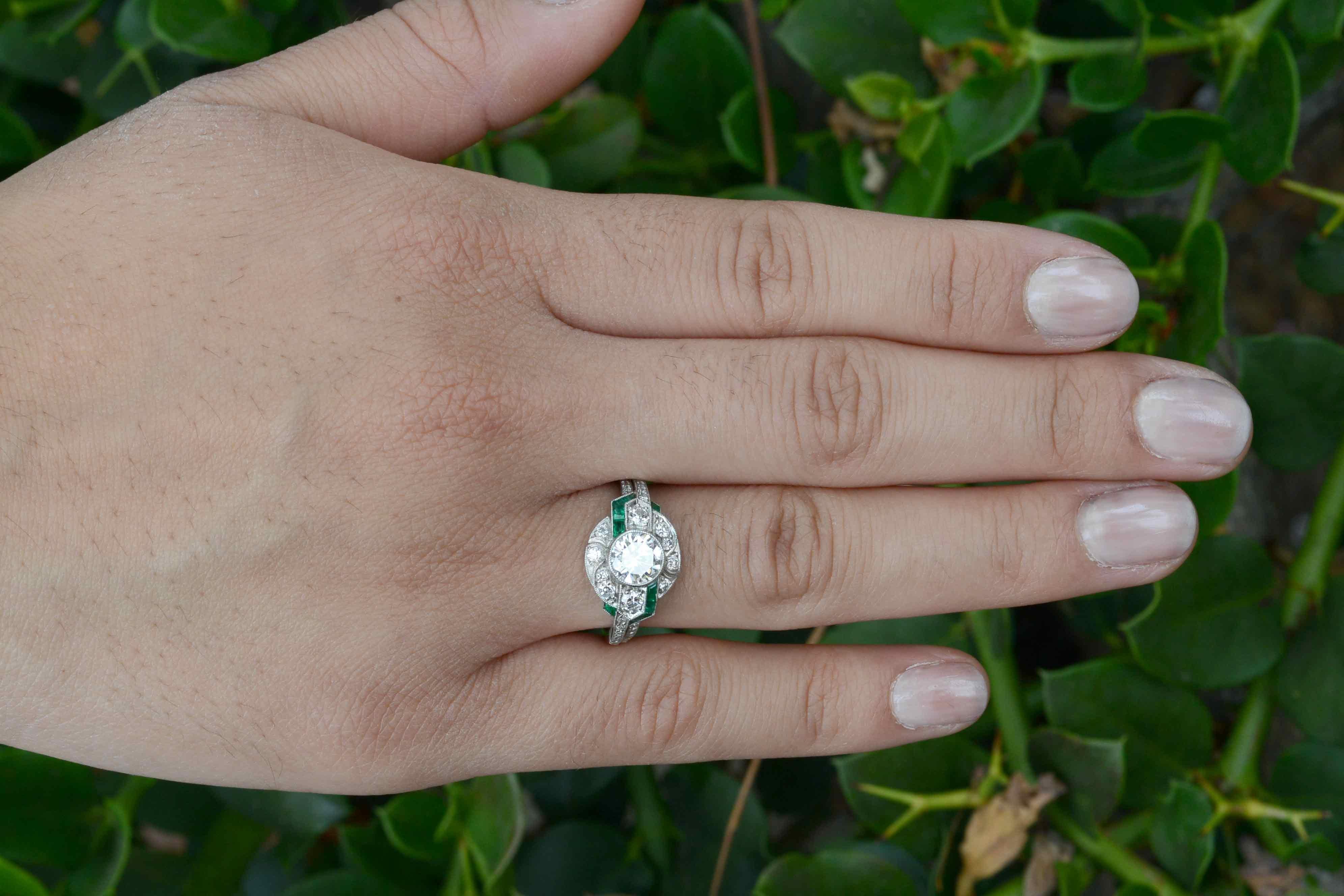 With a fiery sparkle and brilliance that will light up a room, the large, near 1 carat diamond sits regally in a bezel accompanied by a symphony of French cut emerald accents and 38 old cut diamonds. The sleek and angular geometry of this Art Deco