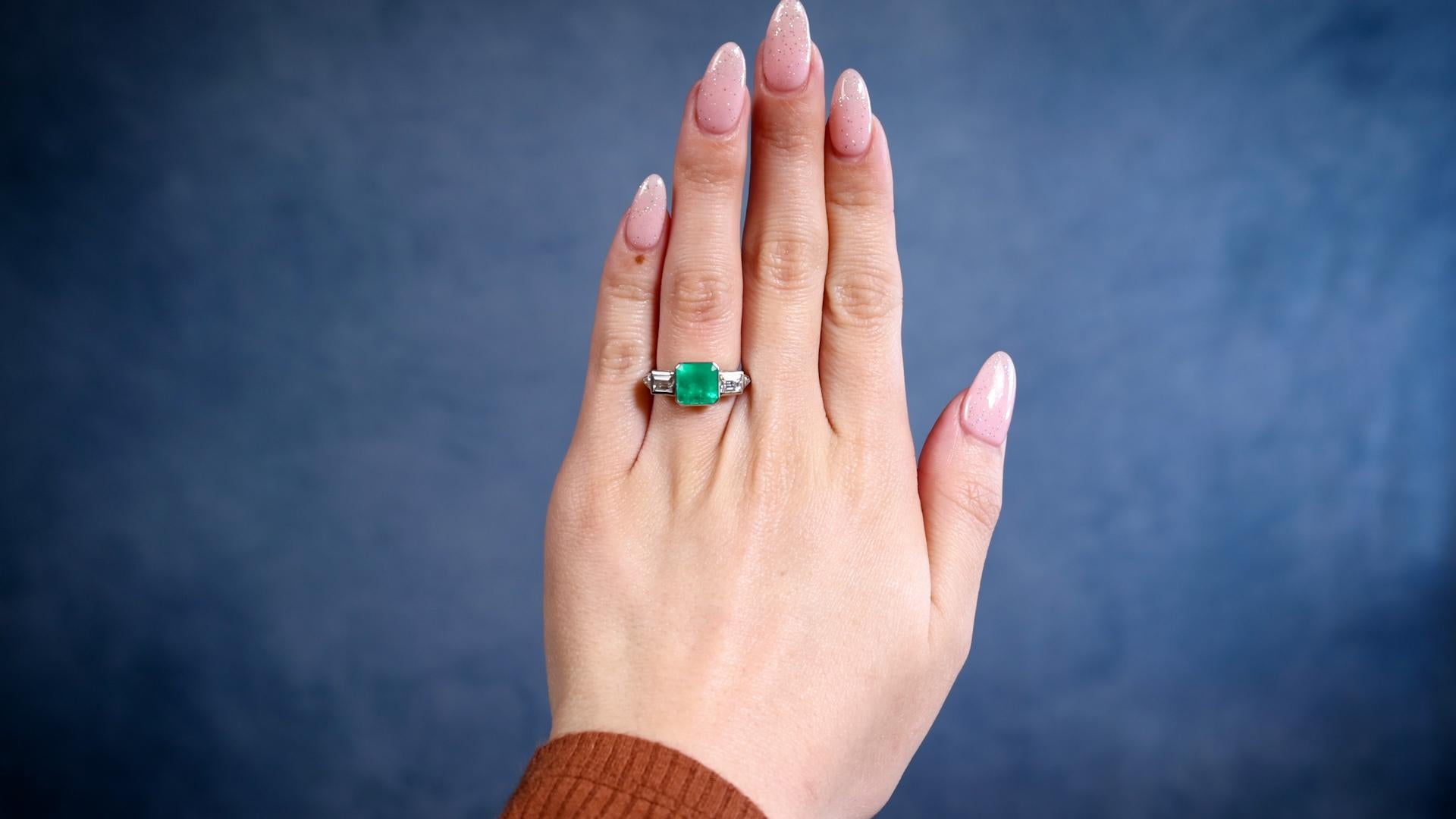 Ein von Art Deco inspirierter Smaragd- und Diamantring aus Platin. Mit einem quadratischen Smaragdschliff mit einem Gewicht von 1,97 Karat. Akzentuiert durch zwei rechteckig geschliffene Carrs und zwei dreieckig geschliffene Diamanten mit einem