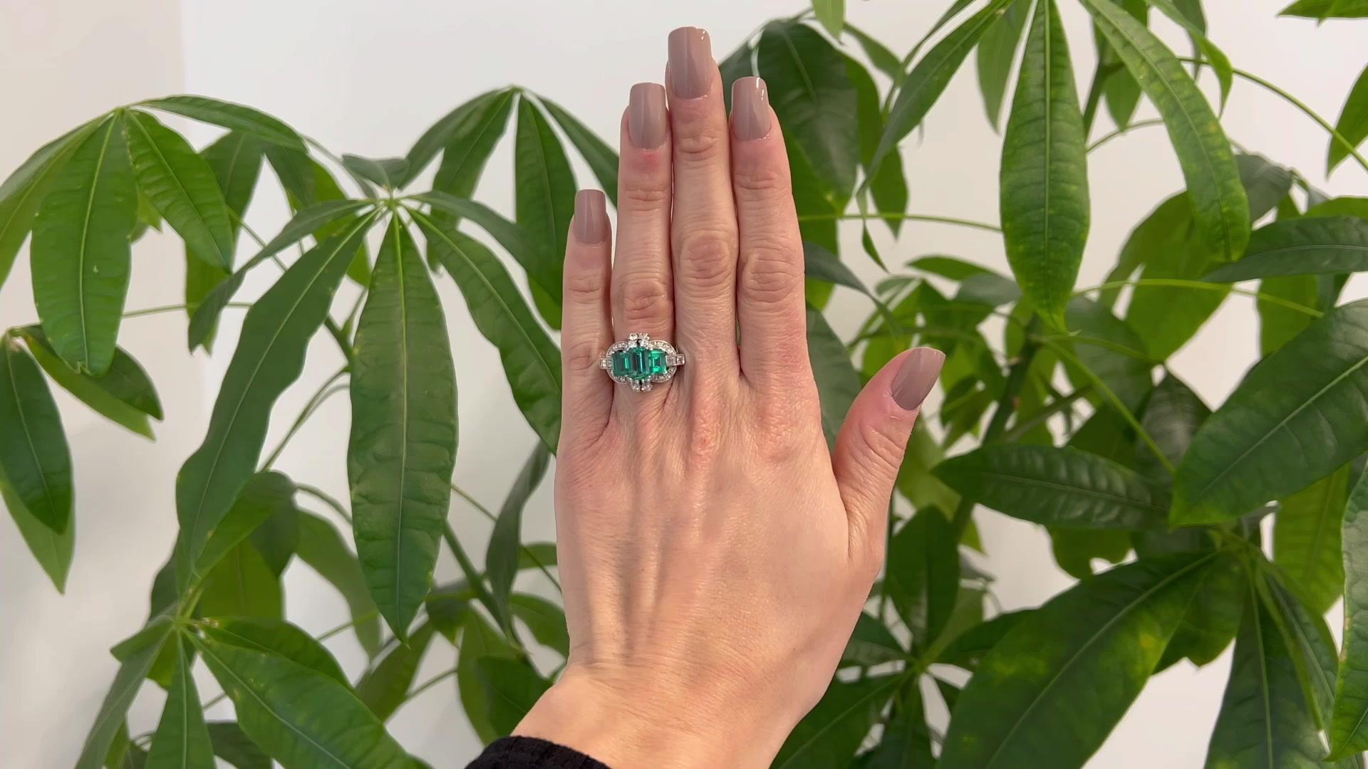 One Art Deco Inspired Emerald Diamond Platinum Cocktail Ring. Featuring three rectangular step cut emeralds with a total weight of approximately 3.00 carats. Accented by 28 single cut, round brilliant cut, and baguette cut diamonds with a total