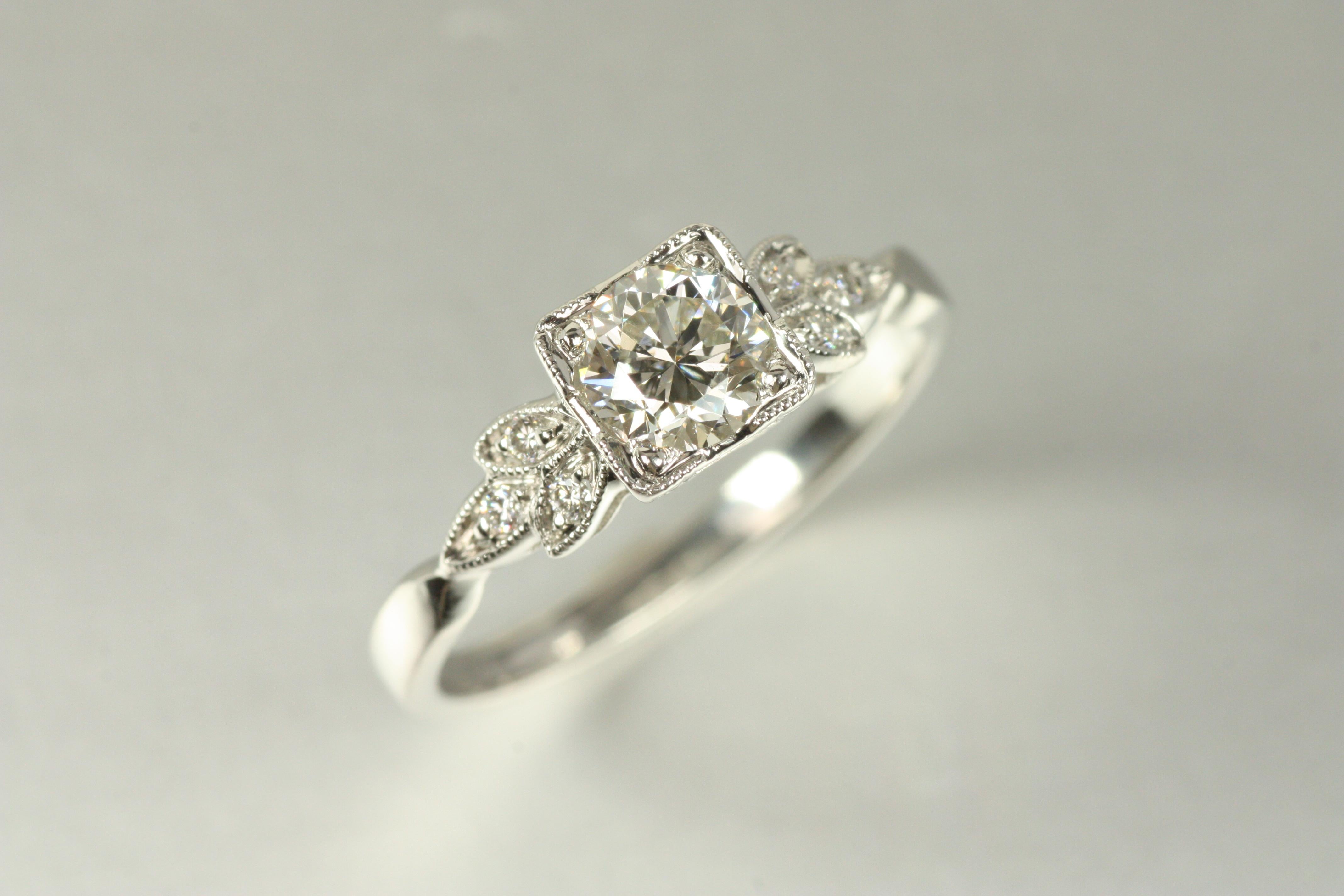Inspired by the elegance of the 1950s, this Art Deco-style engagement ring features a floral motif with vintage milgrain detailing. A 0.57ct round brilliant center diamond is framed by six sparkling round accent diamonds (0.06cttw), adding delicate