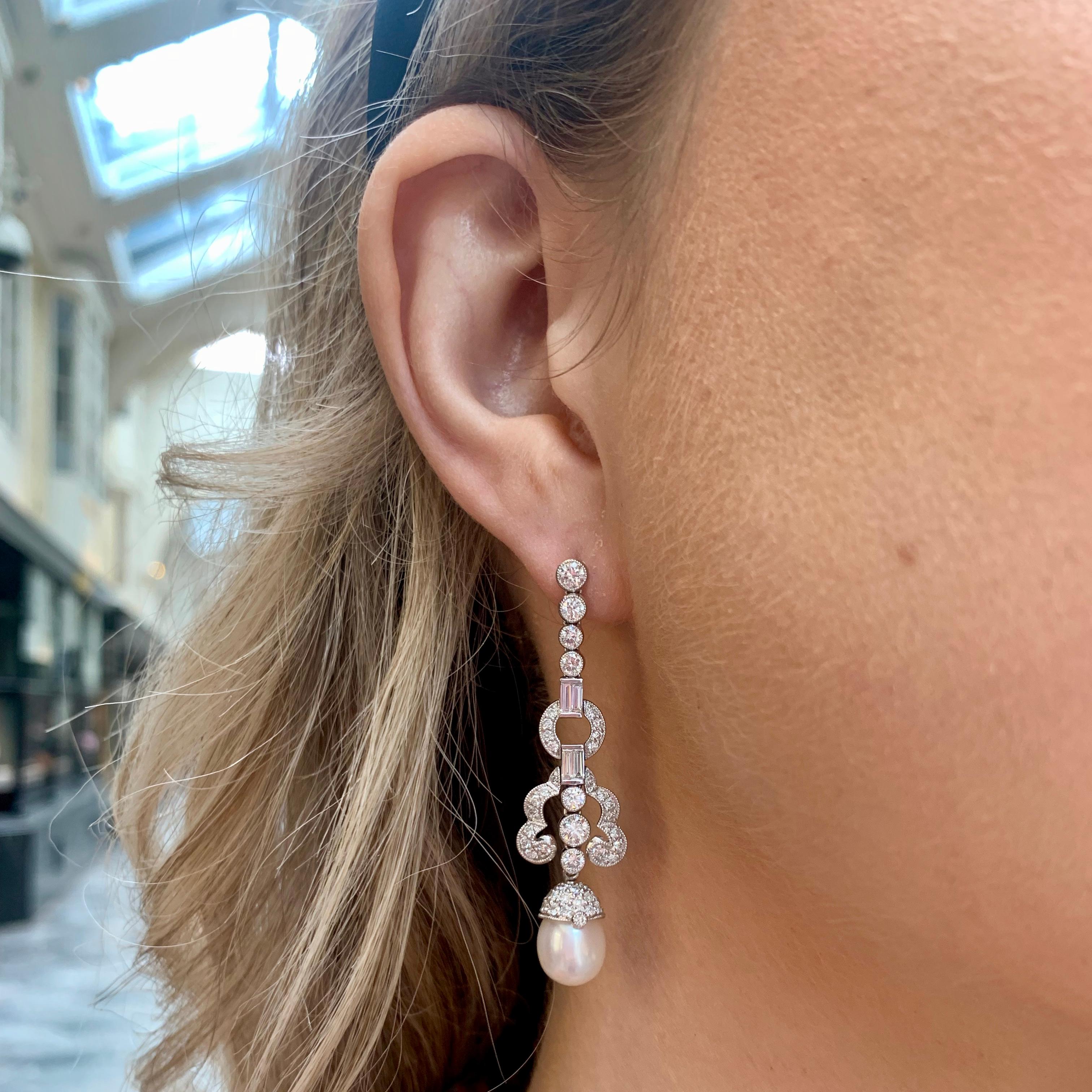 A beautiful pair of Art Deco inspired pearl and diamond earrings set in platinum.

Each earring is firstly composed of a sequence of graduating diamonds, rubover set securely. This leads to two emerald cut diamonds encased in a diamond hoop.