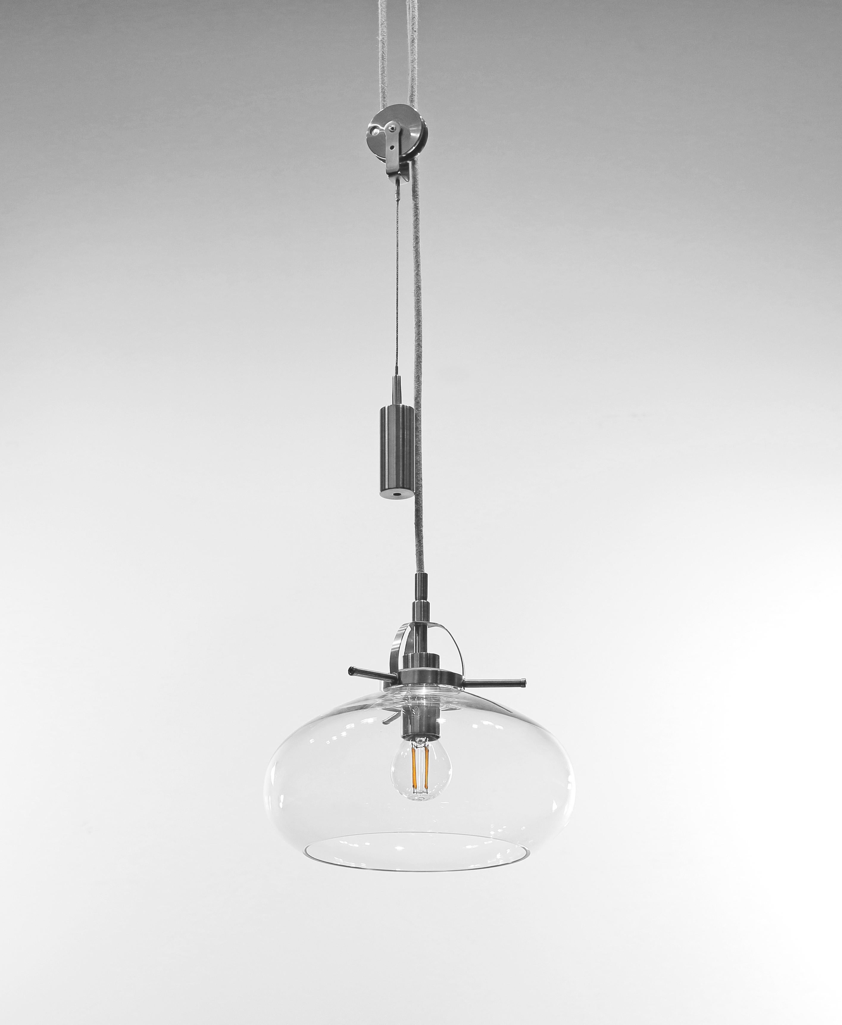 Art Deco-inspired pendant lamp with a weight is crafted with the finest quality materials. This lamp features sleek stainless steel elements and a beautiful clear glass shade that exudes an air of sophistication and elegance.
The lamp boasts a