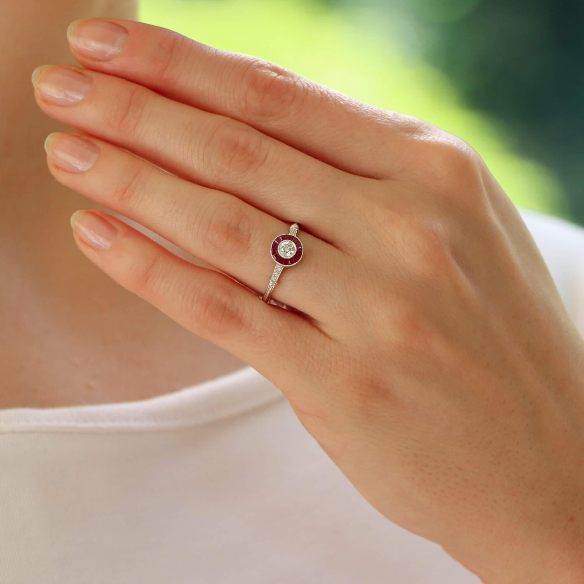 Un bellissimo anello con diamanti e rubini in oro bianco 18 carati di ispirazione Art Deco.

Questo elegante anello è incastonato al centro con uno scintillante diamante rotondo taglio brillante con incastonatura a mille. Il diamante è poi