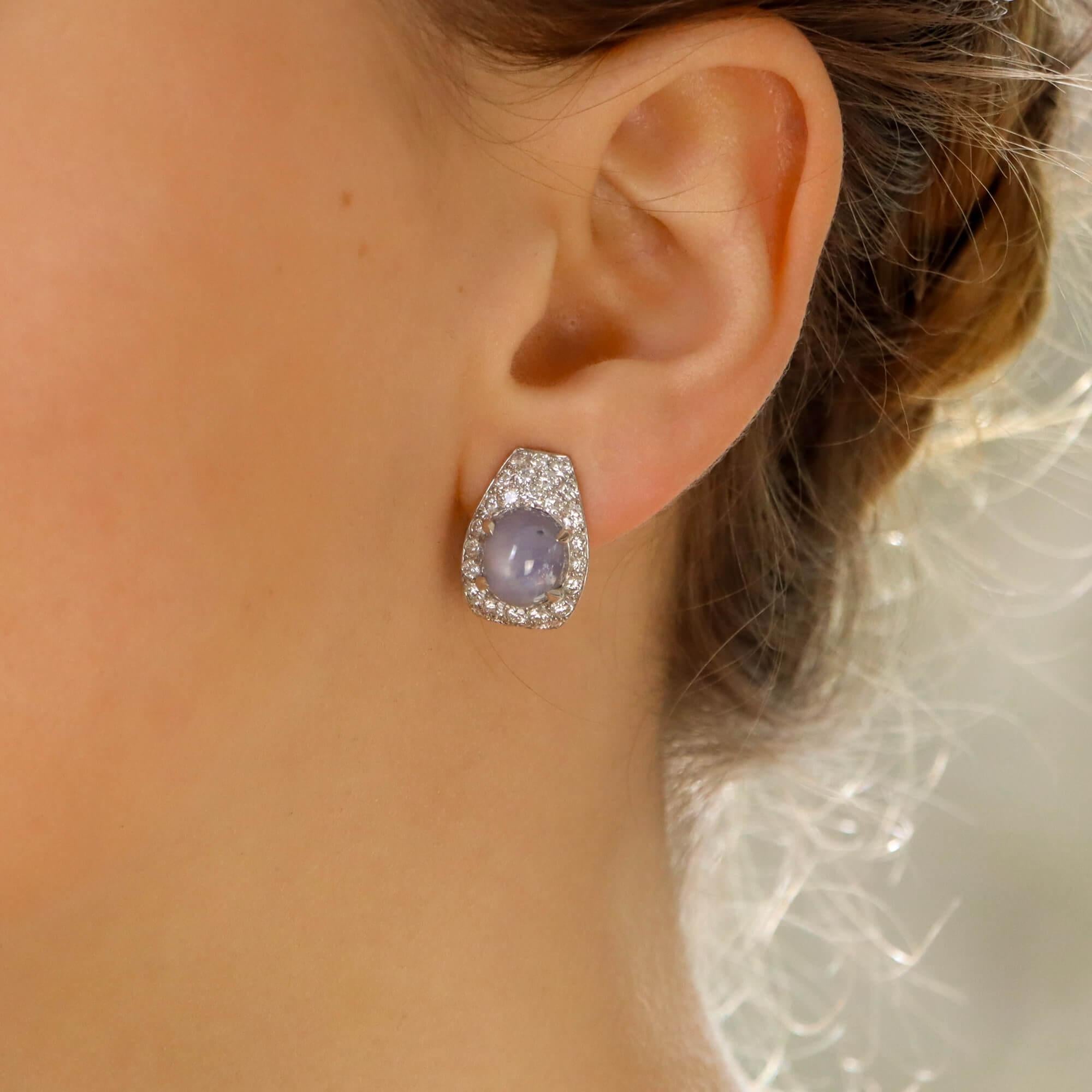 Ein wunderschönes Paar Art-Déco-inspirierter Sternsaphir- und Diamant-Ohrringe aus 18 Karat Weißgold.

Jeder Ohrring ist überwiegend mit einem schönen lilafarbenen Sternsaphir besetzt, der in der Mitte sicher mit vier Krallen gefasst ist. Die