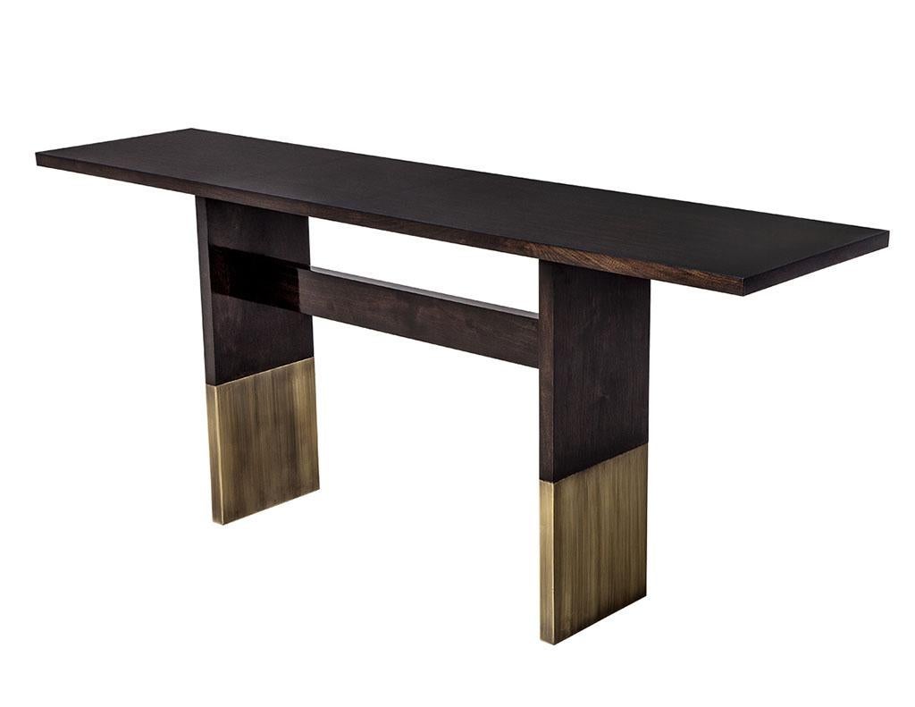 Art Deco inspired walnut console table made by Carrocel. This beautiful hand crafted, made to order console table featuring stunning walnut wood finished with large brass pedestal feet. Available in custom sizes and finishes as desired, pricing will