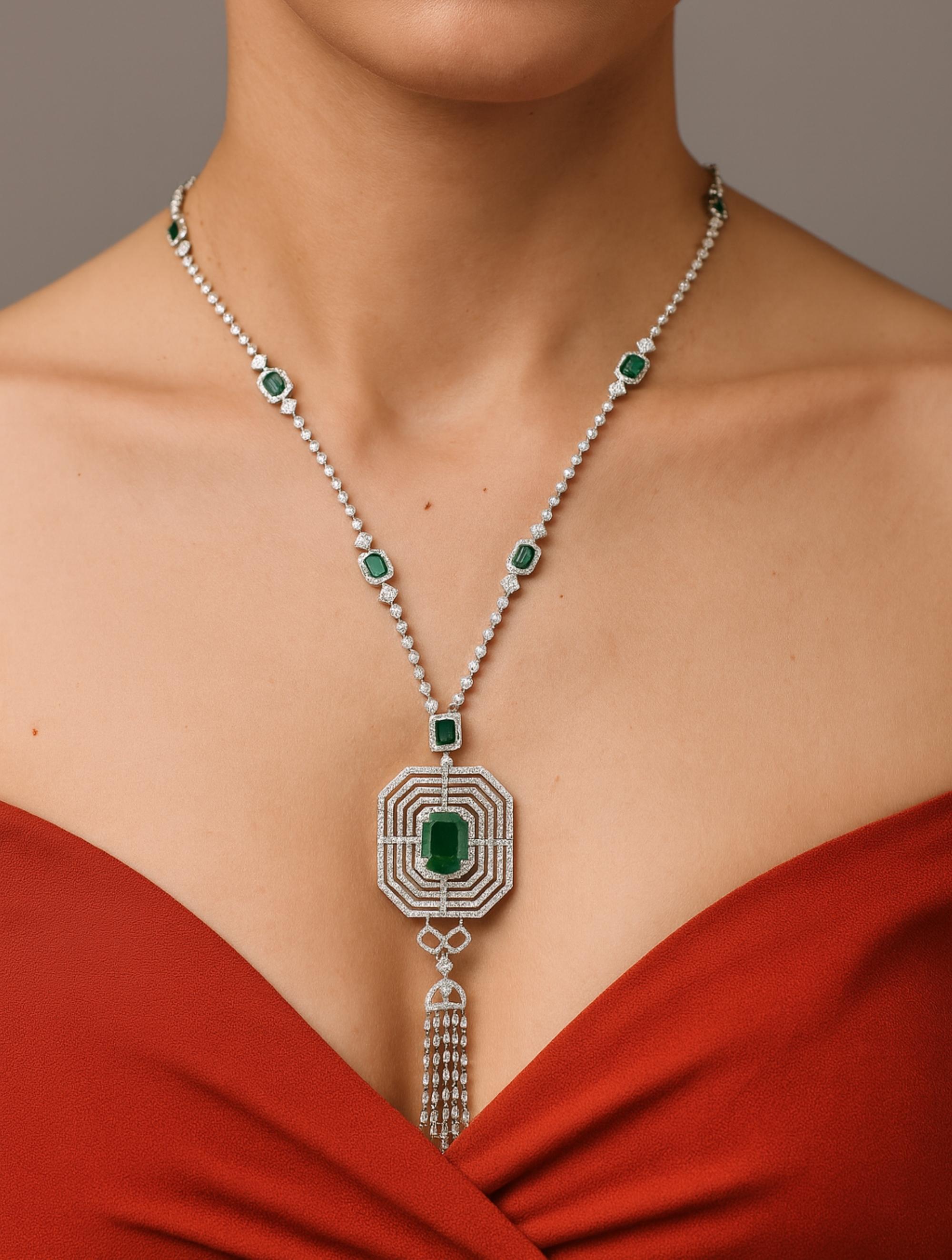 Questa collana di ispirazione Art Deco con smeraldo dello Zambia e diamanti in oro bianco 14 carati è caratterizzata da uno smeraldo con cinque strati di diamanti a raggiera che formano un ciondolo con linee di diamanti che penzolano su una catena
