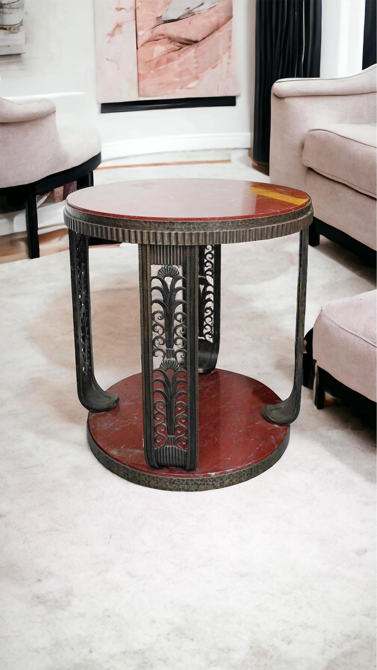 Our Art Deco period center or side table, 37 inches tall and 35 1/2 inches across, features a rouge marble top in iron frame supported by four uprights with stylized organic openwork designs rising from a round marble base with dimpled edge design. 