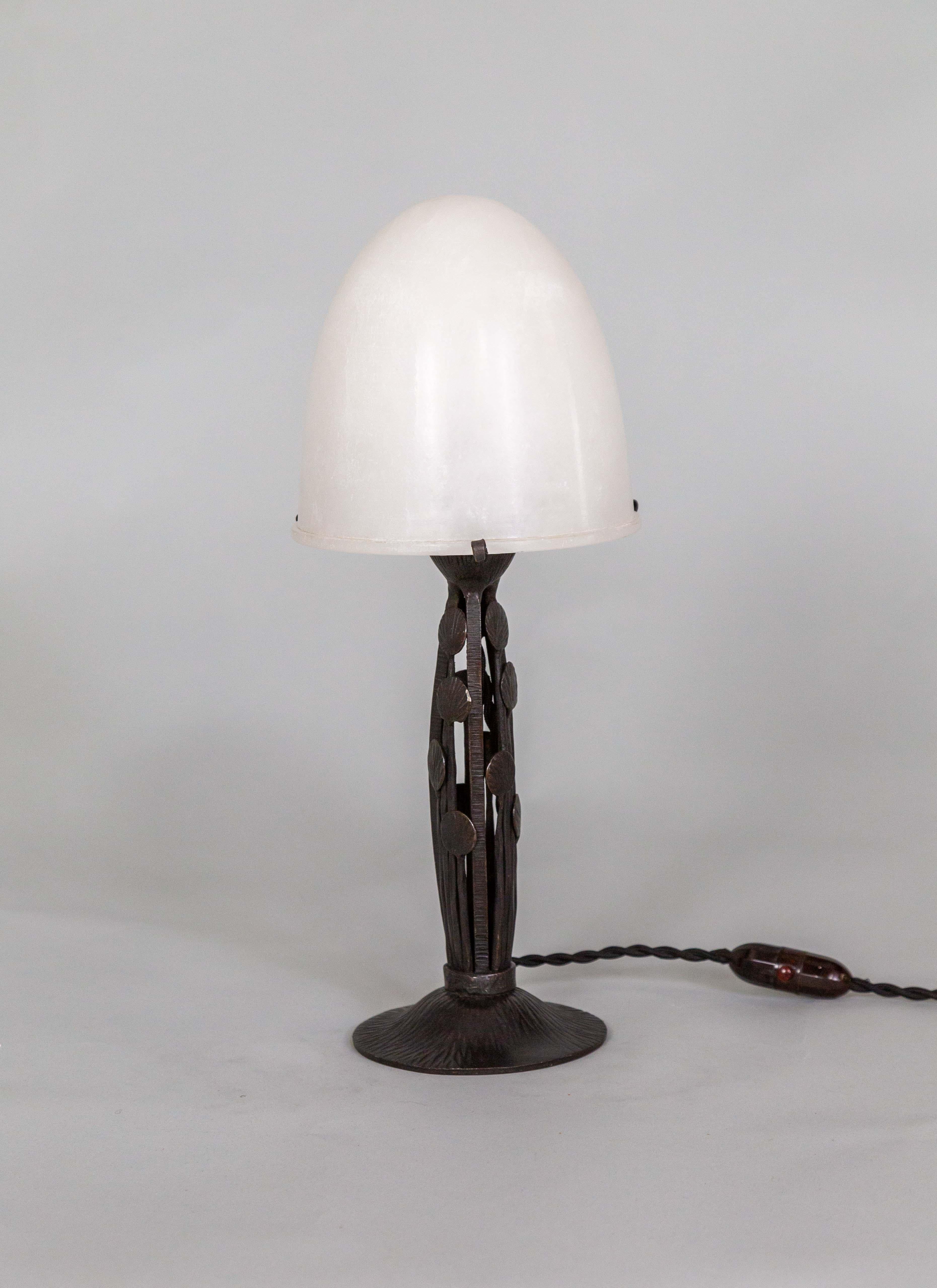 Eine Art-Deco-Tischlampe mit einem schönen Alabaster-Kuppelschirm, der auf einem mit Muschelformen verzierten Eisenfuß sitzt. Verdrahtet mit einem Inline-Schalter und einem Seilkabel; Stecker Typ C mit Adapter Typ A. Hergestellt in Frankreich um