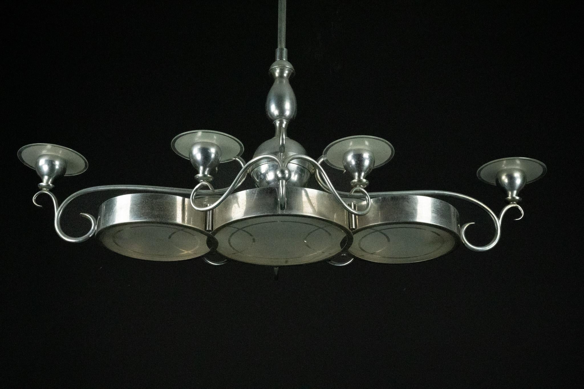 Eleganza e rarità del lampadario Art Deco italiano risalente alla fine degli anni '30-inizio anni '40. Realizzato in metallo nichelato spazzolato, il lampadario presenta sei diffusori in vetro smerigliato integrati in una struttura centrale