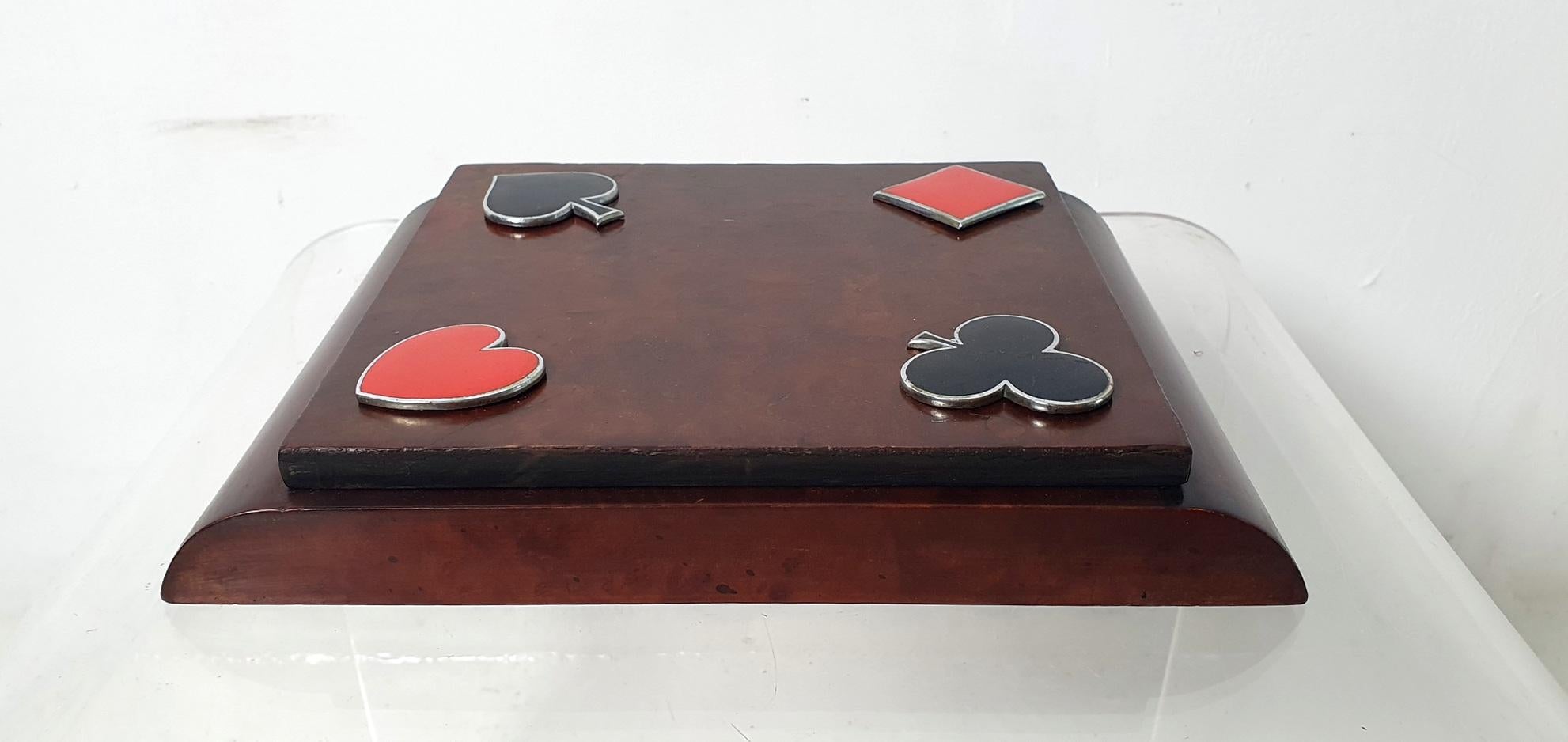 Eine Schachtel für Spielkarten aus Ahornholz mit Chromdekor und emaillierten Symbolen für Pik, Herz, Nelke und Karo. Die Schachtel hat einen Klappdeckel und im Inneren befinden sich drei Fächer. Dieses Stück wurde in den 1930er Jahren in Italien