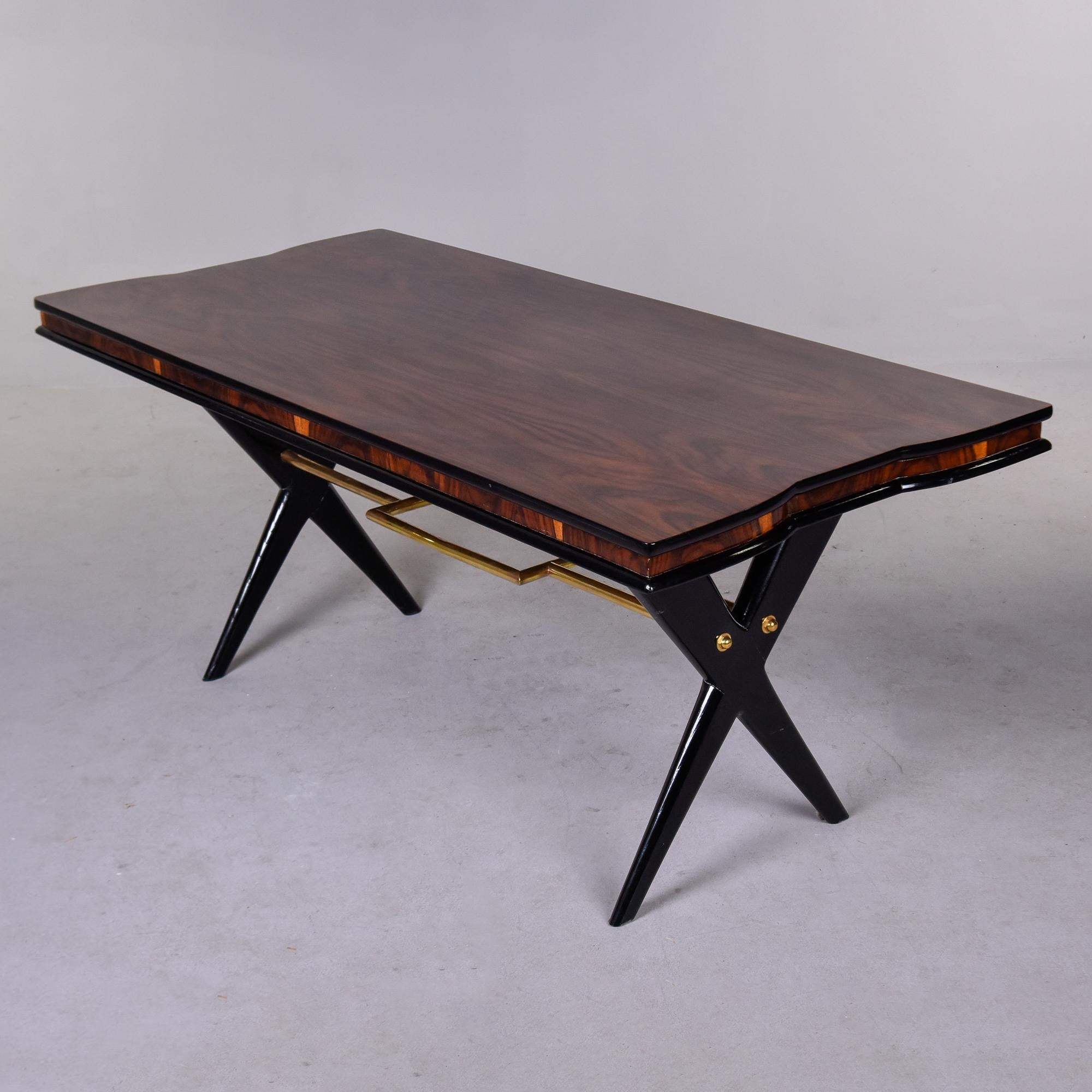 Trouvée en Italie, cette table de salle à manger Art déco datant de 1950 a des pieds noirs en forme de X, un châssis décoratif en laiton avec des détails rectangulaires et un plateau en bois de rose avec des courbes subtiles à l'extrémité. Cette