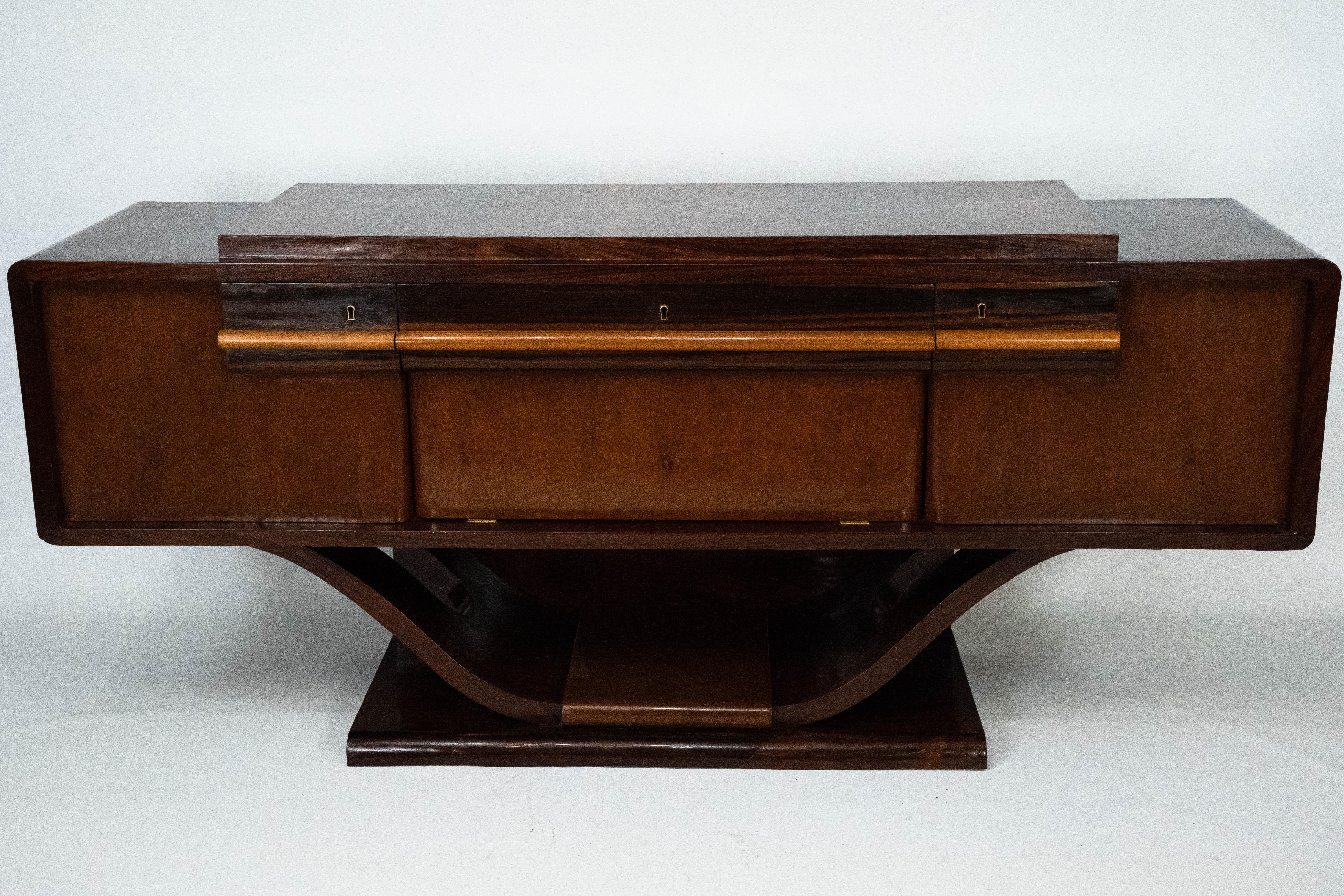 Elegant buffet italien Art Deco des années 1920, présentant les lignes raffinées et les volumes sculpturaux typiques du début du design Deco. La pièce présente un beau contraste entre la structure polie foncée et les panneaux avant plaqués plus