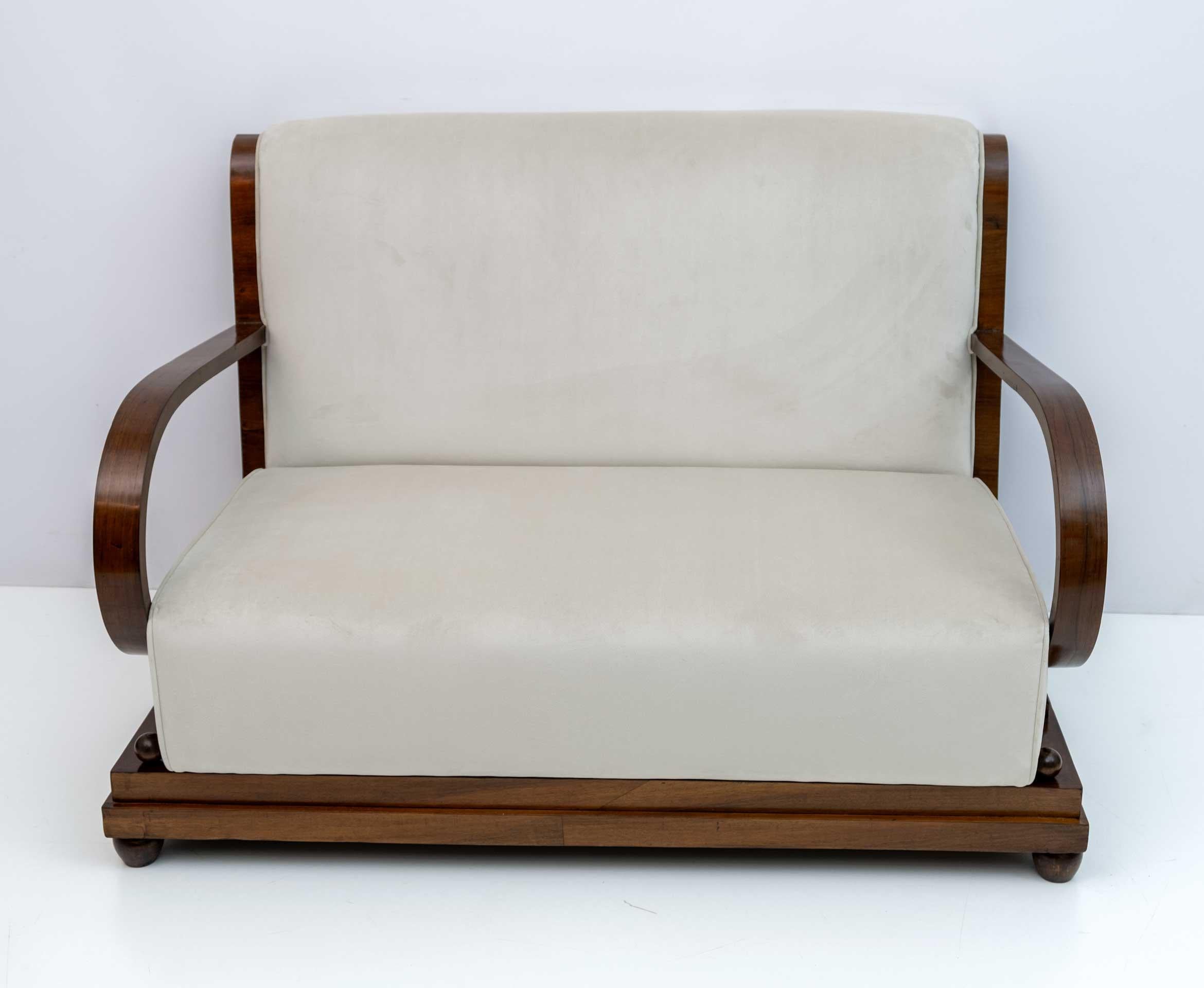 Divano del primo periodo Art Deco dell'Italia settentrionale, in noce e con rivestimento in velluto color avorio; lo schienale del divano è graziosamente curvo e si estende per accentuare la curvatura dei braccioli inclinati. Recentemente è stato