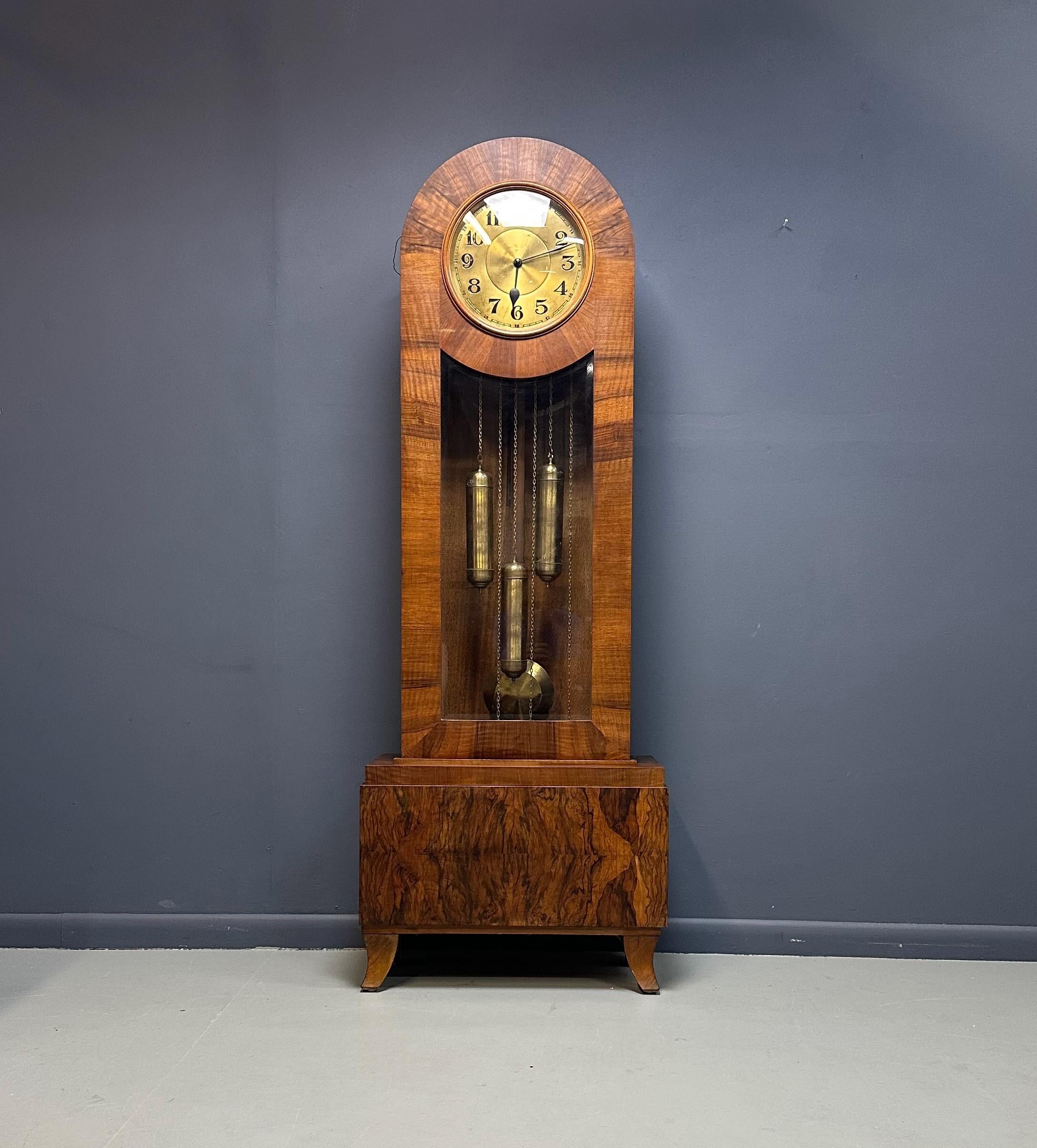 A striking Art Deco J. Brandmann grandfather clock, crafted circa 1930s, showcasing the elegance and geometry of the period. The case features rich walnut veneer with beautifully figured grain, softened by rounded edges and a gently arched hood. Its