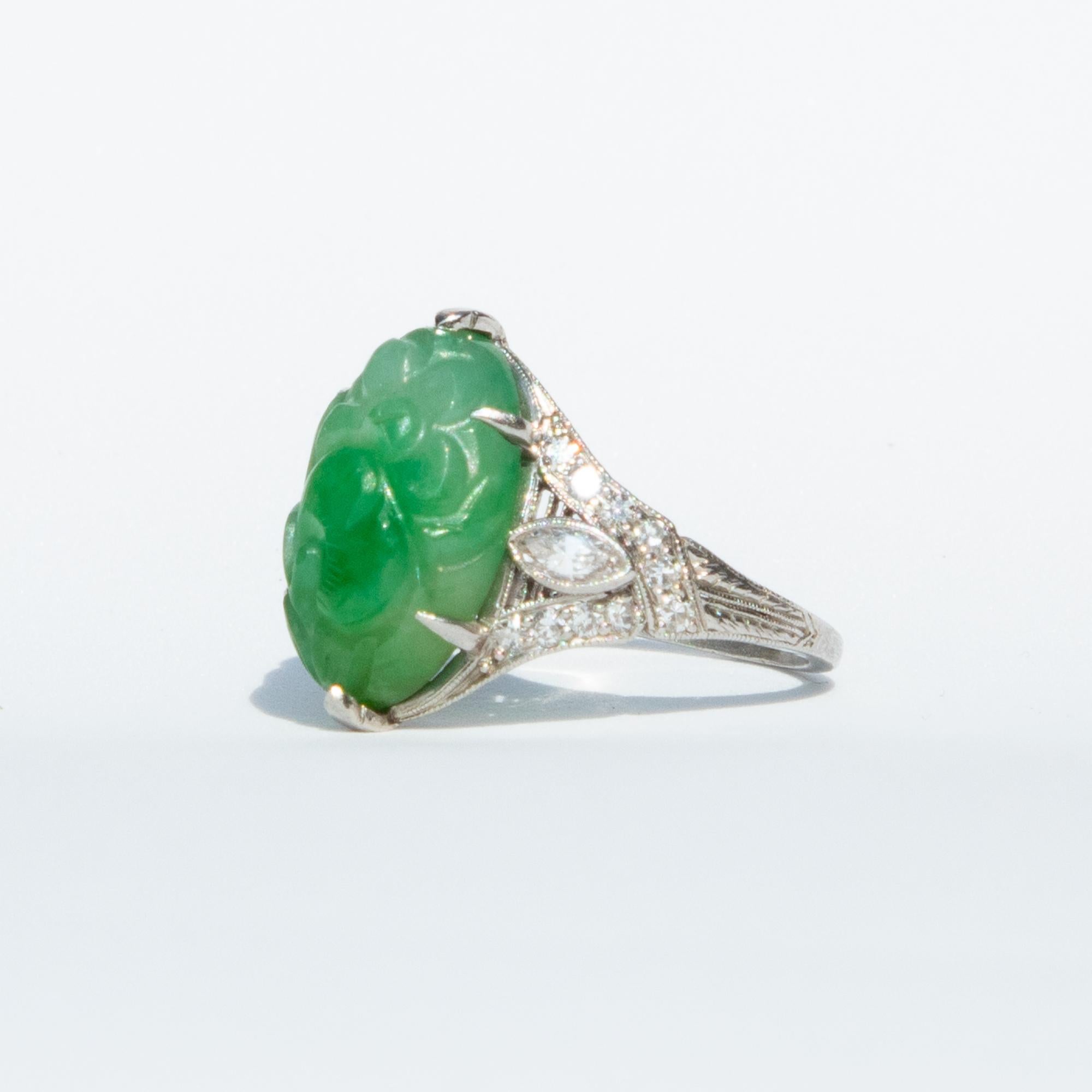 A beautiful jade and diamond ring from the Art Deco era. This rind boasts a large hand-carved jade flanked decadent diamond encrusted shoulders, set in platinum. Total diamond weight certified 0.7 carats, H colour and SI-1. 

The carved Jade is