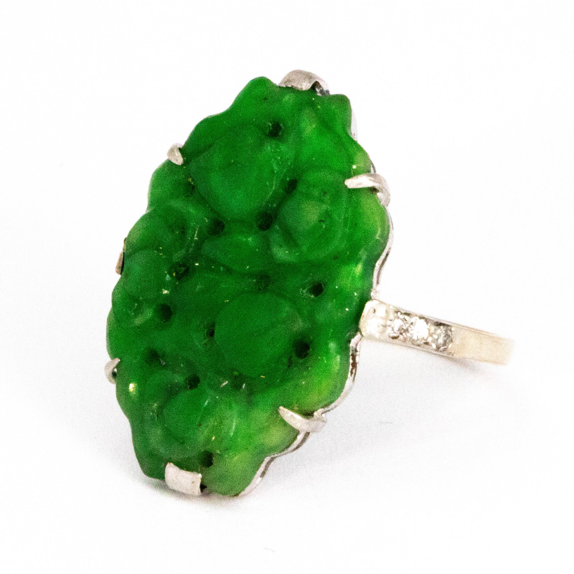 This gorgeous bright green jade stone is simply set in claw settings and the stone itself is exquisitely engraved. The shoulders of the ring hold three small diamonds each. The back of the main stone and the side of the shoulders feature open work