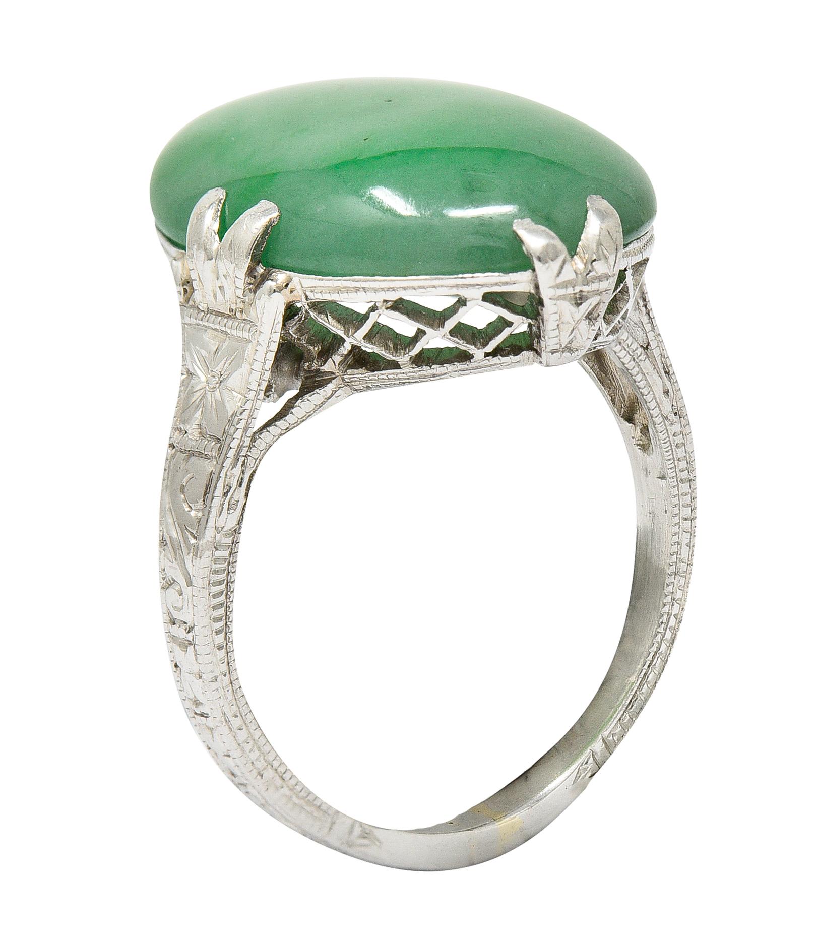 Featuring an oval jade cabochon measuring approximately 15.5 x 11.5 mm. Translucent and moderately mottled green to light pastel green. Set by split prongs with a pierced trellis motif gallery. Shoulders and shank are engraved with a stylized and