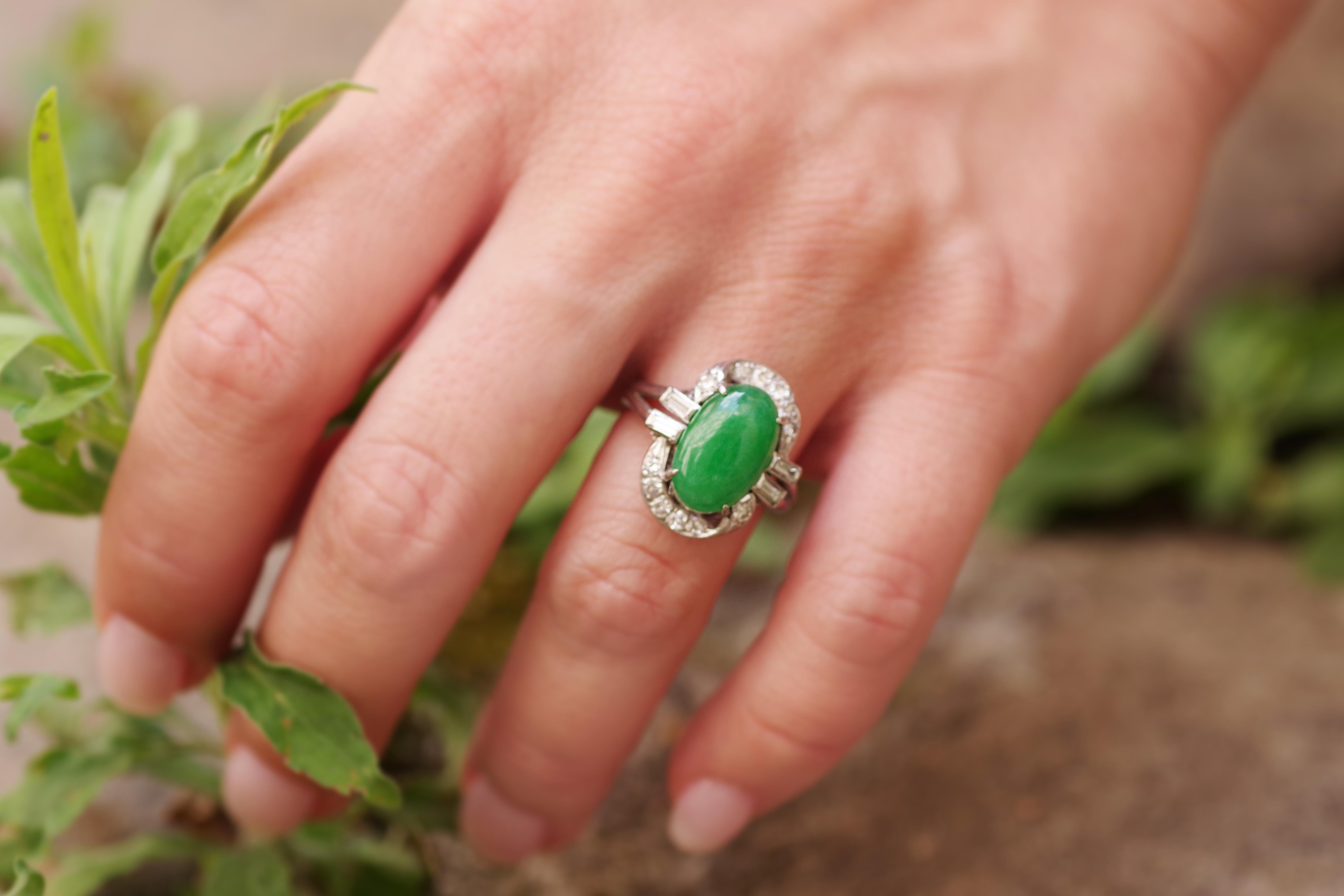 Art Deco Jade diamond ring in 14 karat white gold. Elegant ring set with an oval cabochon of jade jadeite of a beautiful intense green colour with slightly white veins. The gem is set with four claws and surrounded by twelve single-cut diamonds on a