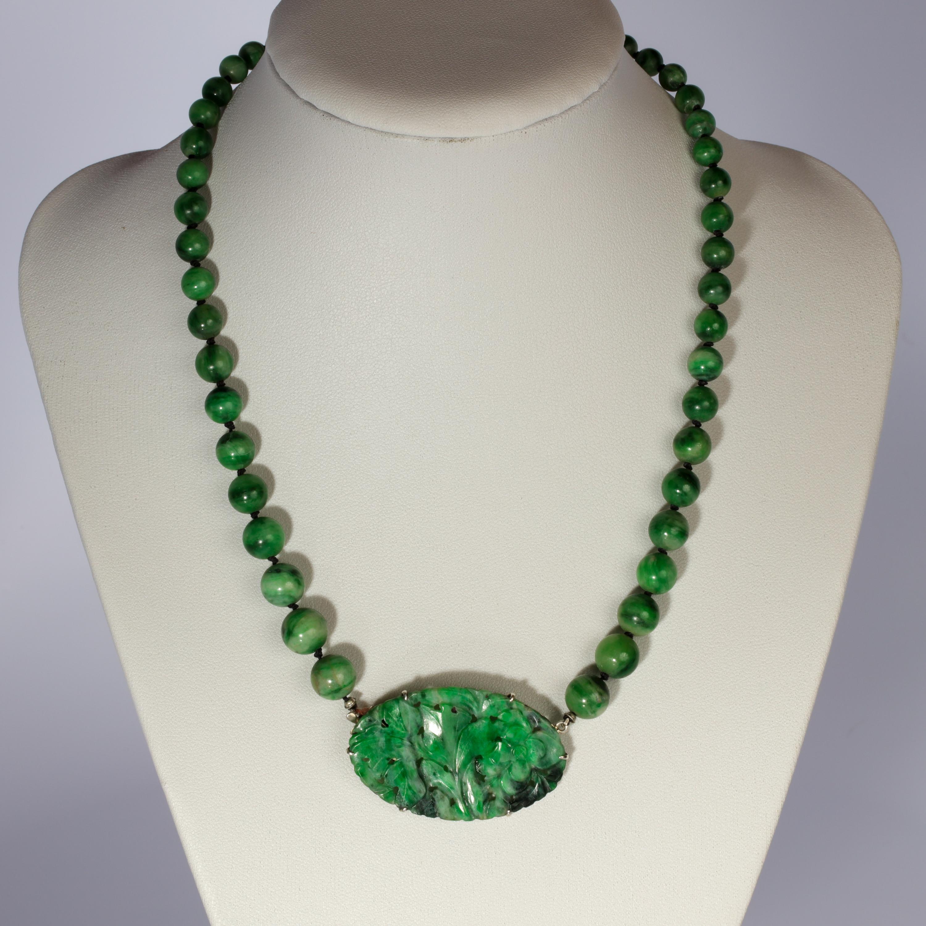 This richly saturated variegated green jadeite necklace was created around 1910 from 100% natural and untreated jadeite jade from Burma. The beads were each hand-carved and polished and the central plaque was carved in a floral motif. The necklace