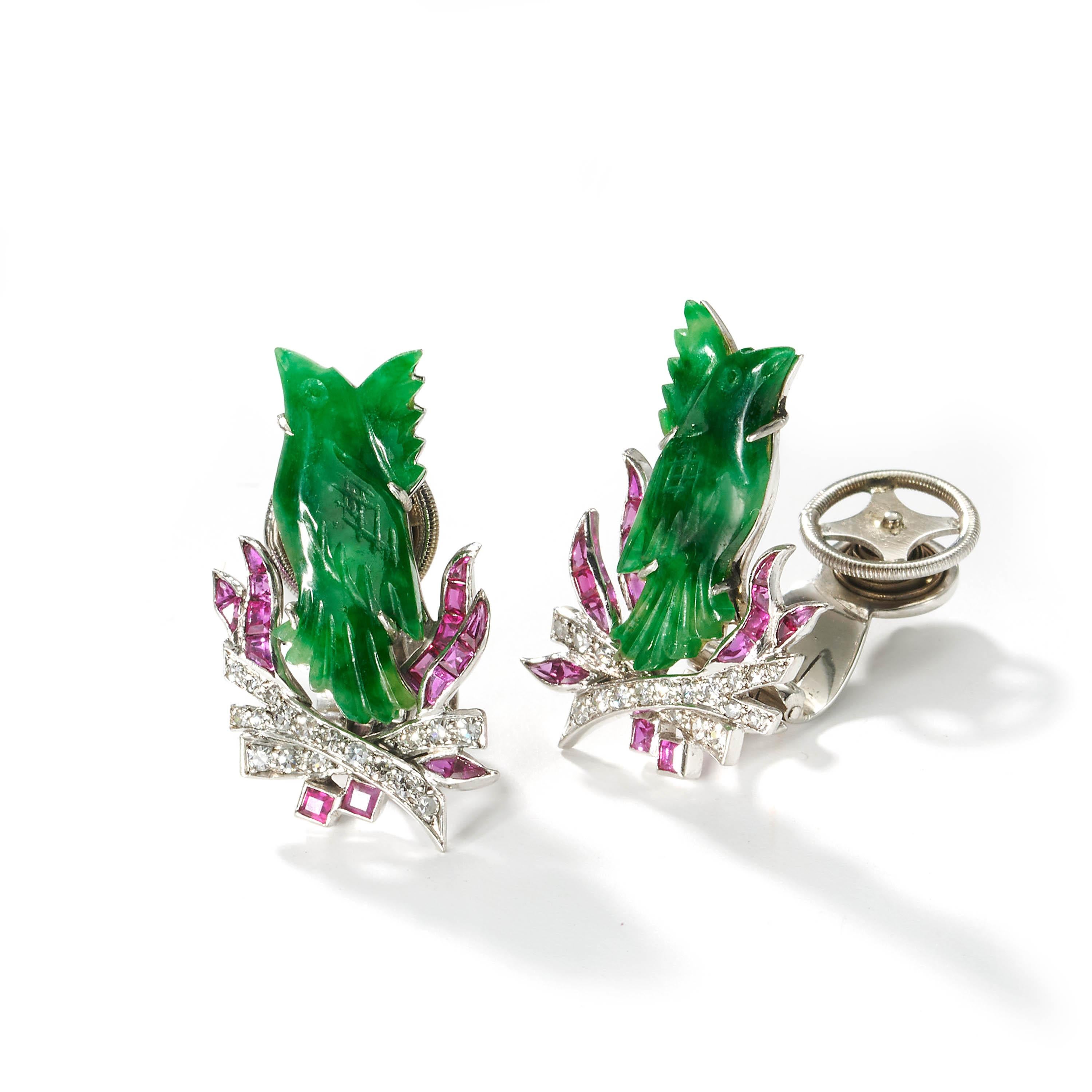 A pair of Art Deco jade, ruby and diamond earrings, set with jadeite jade carved Chinese phoenix birds, on eight-cut diamond set branches, with calibré cut ruby, channel set flames, mounted in platinum, with white gold clip-on fittings, with sprung