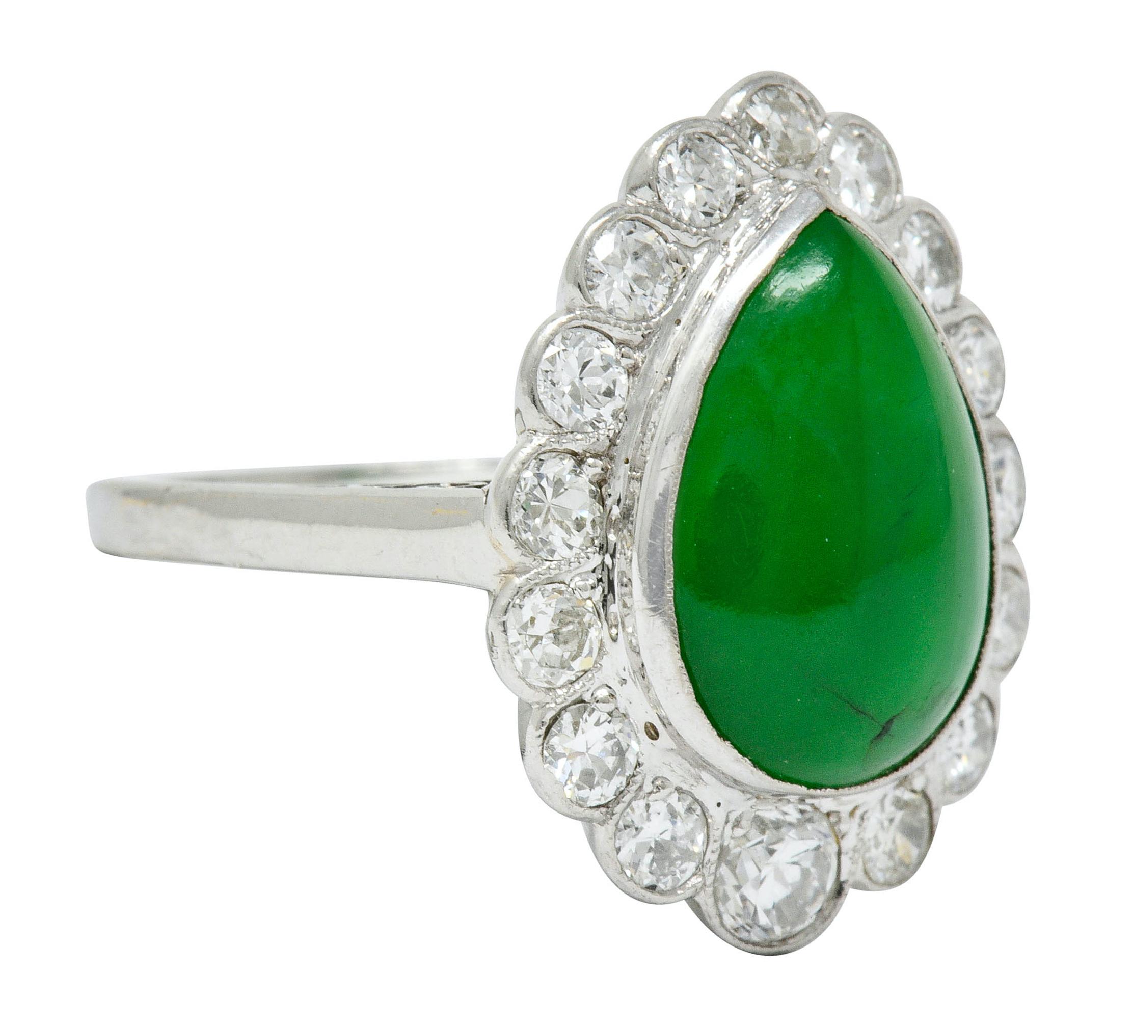 Cluster style ring centering a bezel set pear jade cabochon measuring 13.4 x 9.5 mm
Type A jadeite jade with no indication of impregnation, translucent with a deep and even green color

Surrounded by round brilliant cut diamonds weighing