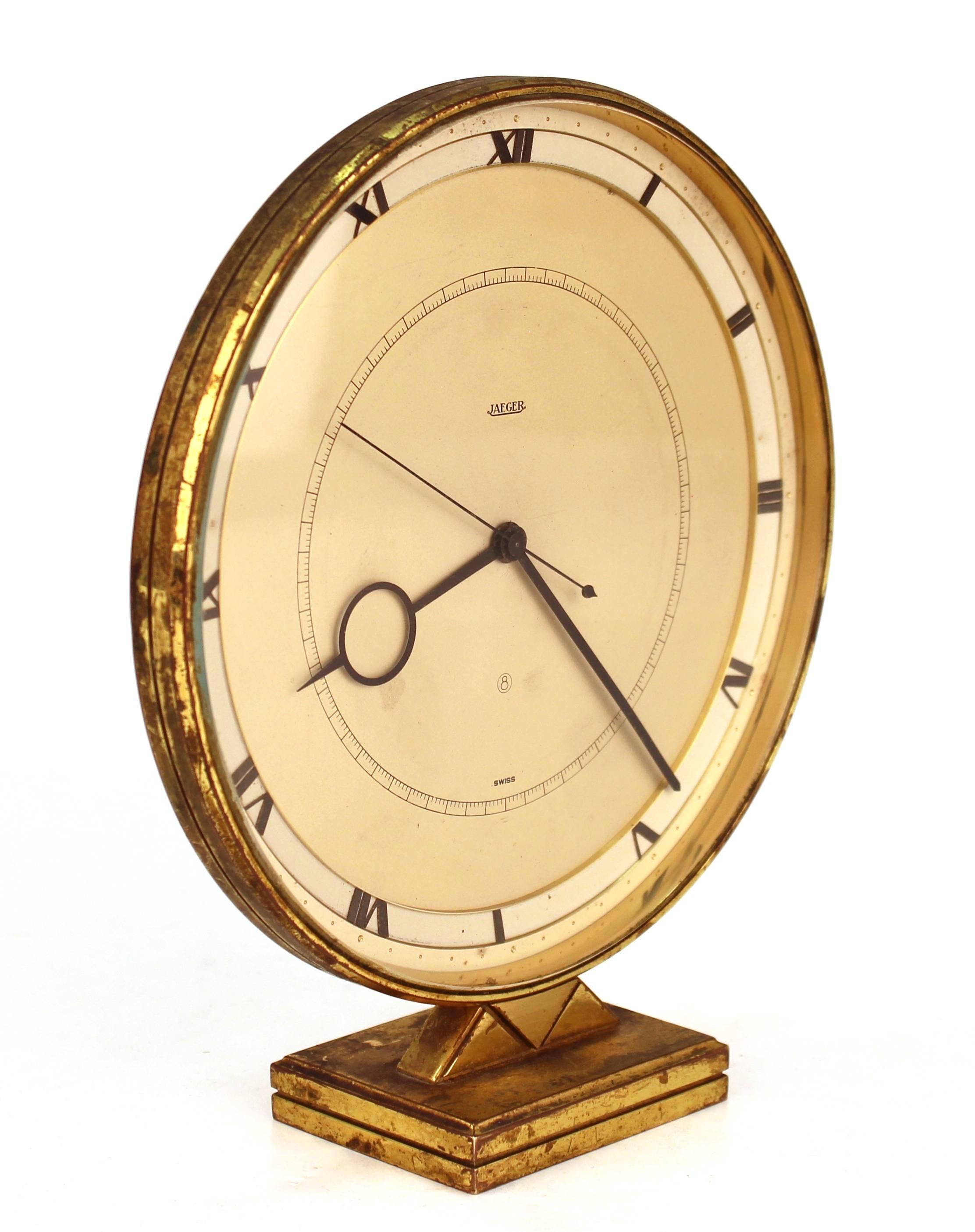 Jaeger-LeCoultre table or desk clock dating in the Art Deco style from 1920s-1930s Switzerland. Features a round face set into a brass frame with a triangular Deco pattern stand and rectangle base. The piece runs perfectly without rewinding for five