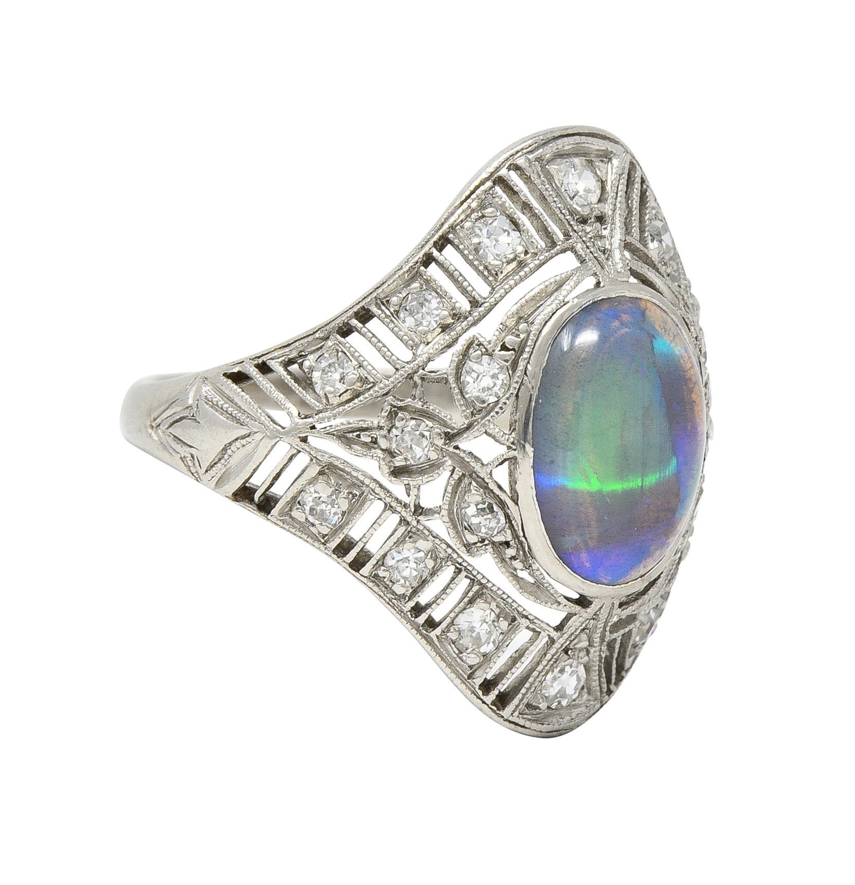 Centering a bezel set oval-shaped jelly opal cabochon measuring 7.0 x 9.0 mm 
Transparent black body color with strong blue, green, and violet flashing 
Featuring a navette-shaped and pierced lotus motif filigree surround 
Bead set with single cut