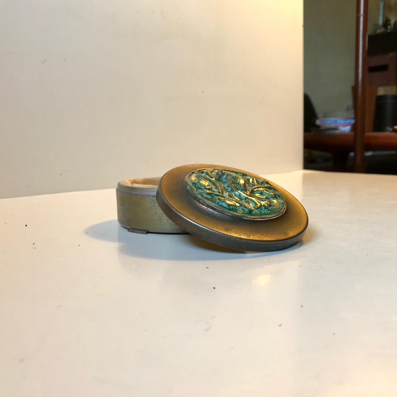 Kleines, ungewöhnliches Schmuckstück mit Bronzedeckel, besetzt mit einer keramischen Relieftafel mit einem grünen Papagei/Sittich in kristalliner Glasur. Der untere Teil des Gefäßes ist wahrscheinlich aus Zinn gefertigt. Dieses Stück ist mit BL