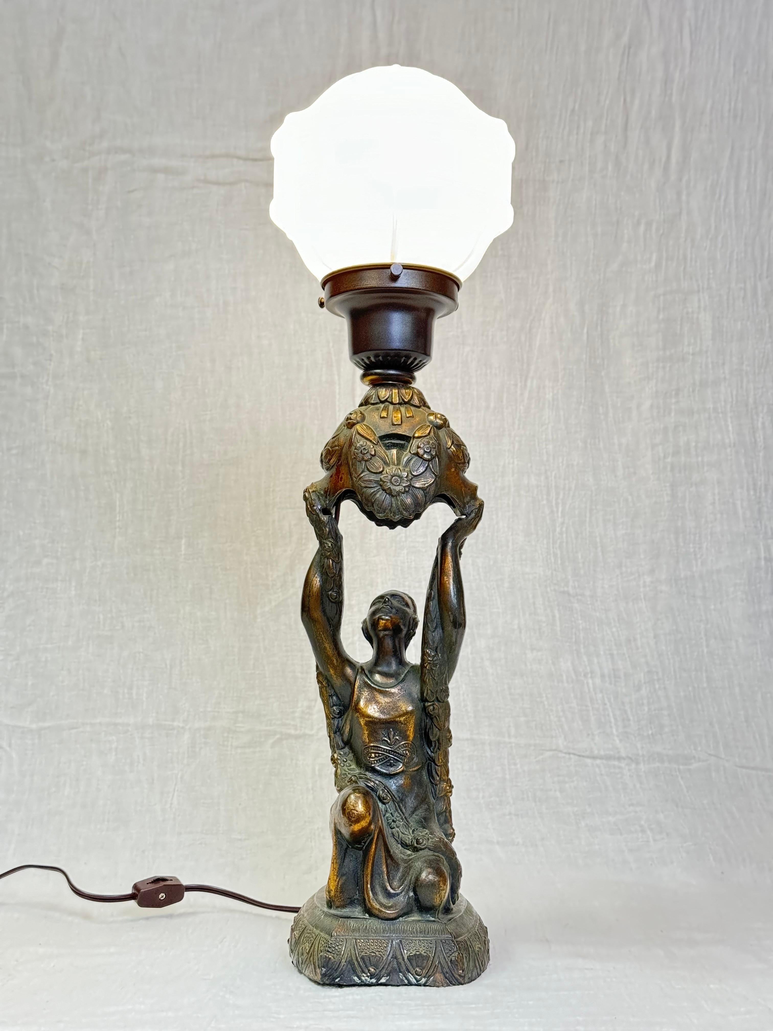   Art Deco Bronze style table lamp of Joan of Arc . This classic 1910 lamp by La Belle depicts Joan of Arc holding up a bouquet and kneeling on a pedestal . This lamp is made of spelter and has a milk glass shade. This lamp has been newly rewired. 