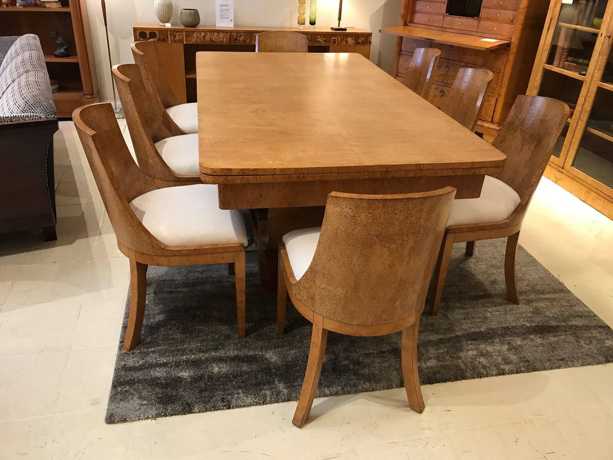 Magnificent Karelian Birch Art Deco dining table with two extensions. With eight matching solid curved back chairs which have been reupholstered in a macro suede fabric. The table has a curved support which rests on a shaped base.
When fully
