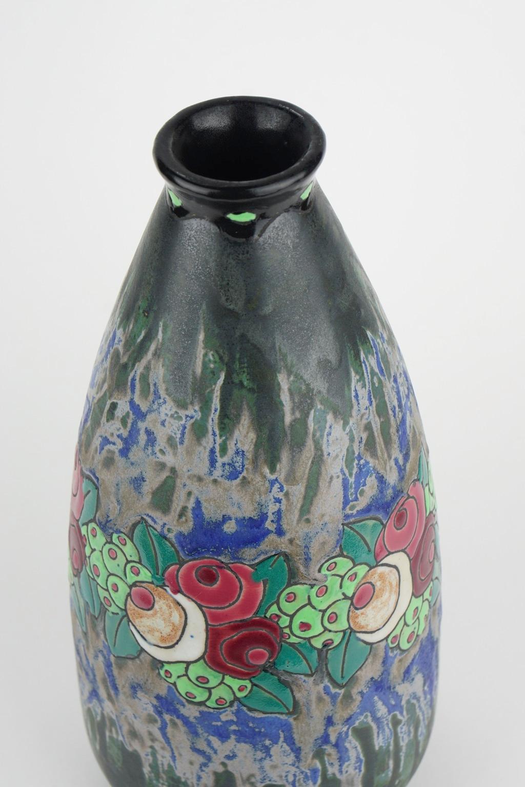 This Art Deco Keramis stoneware vase has a polychrome design with a garland of stylised small roses, leaves and fruits in a blue and dark green background. D 700. F 898. Charles Catteau (1880-1966).

Size: Height 31.2 cm, diameter base 9.9 cm,