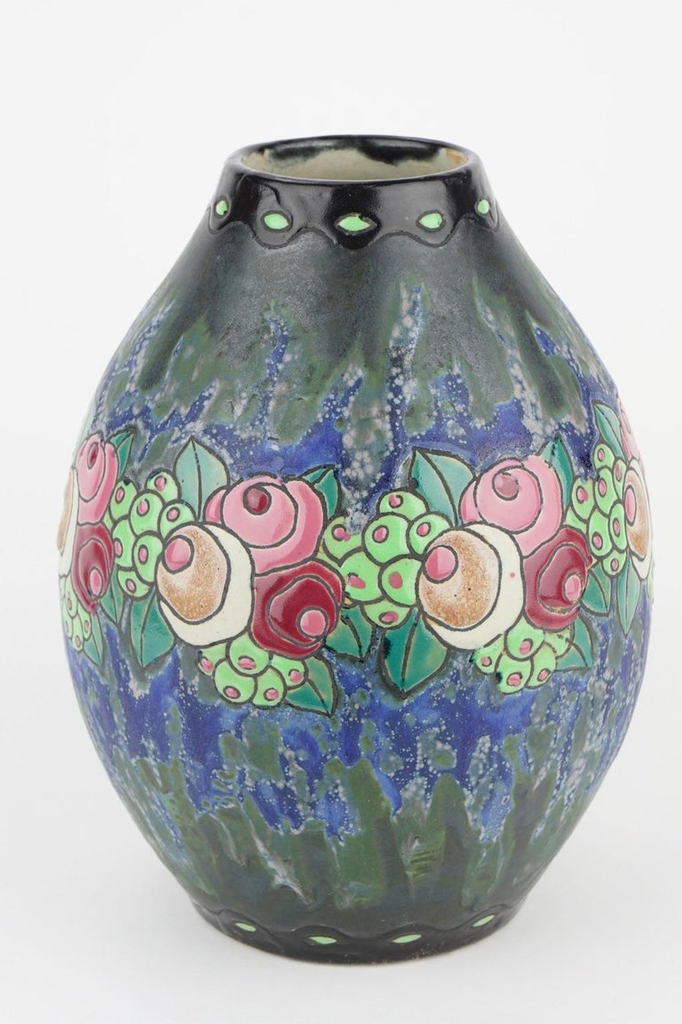 This Art Deco Keramis stoneware vase has a polychrome design with a garland of stylised small roses, leaves and fruits in a blue and dark green background. D 700. F 901. Charles Catteau (1880-1966).

Size: Height 24.5 cm, diameter base 11.5 cm,