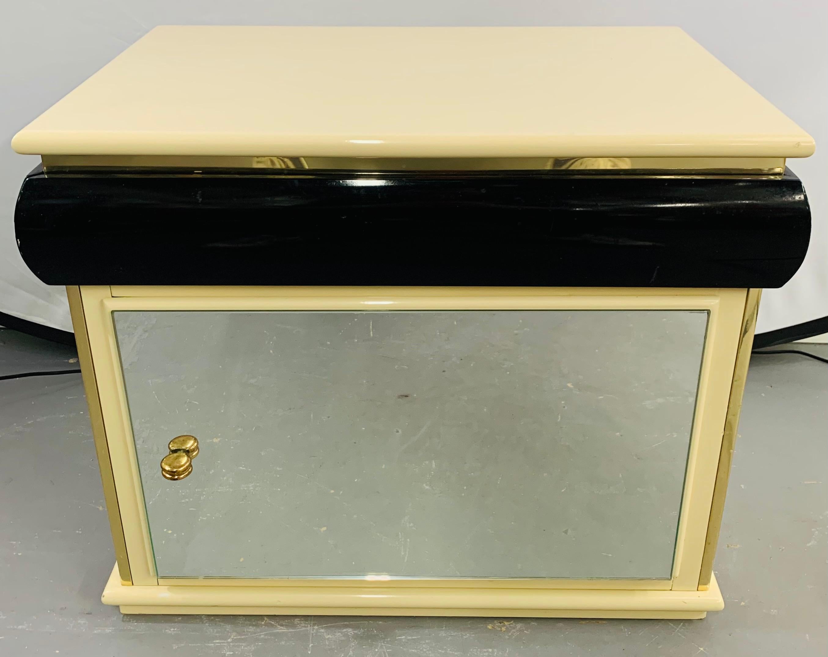 A timeless pair of Art Deco lacquered off-white and black nightstands or side tables with brass frames and original brass knobs. The doors are mirrored which makes this pair of nightstands very stylish. 

Some scratches to the surface but overall