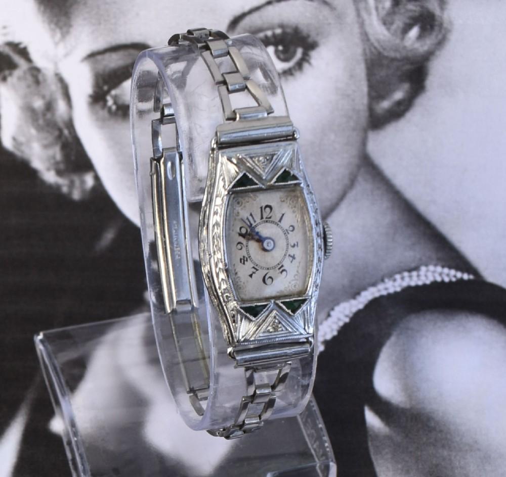 For your consideration is this truly beautiful ladies original Art Deco manual wrist watch with original strap. The main case is 14k white gold filled with triangular synthetic emeralds as accents. Heavy art deco decorative engraving to the case and