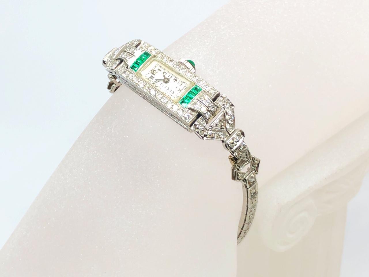 An Art Deco diamond and emerald cocktail watch, set with four calibré-cut emeralds to each shoulders and diamond set case and bracelet. Mounted in Platinum. Circa 1930.