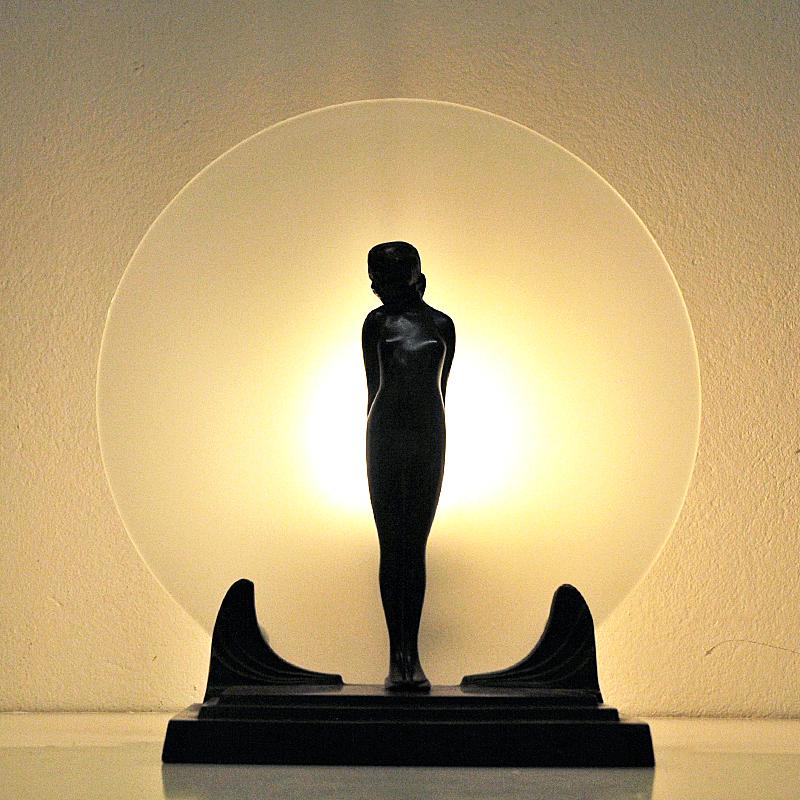 Lovely Art Deco table lamp of patinated bronze and a frosted glass plate on the back. A bronze lady statue in front on a bronze base with a frosted glass plate placed as a feather behind. Gives a beautiful, light and atmosphere in your home.
