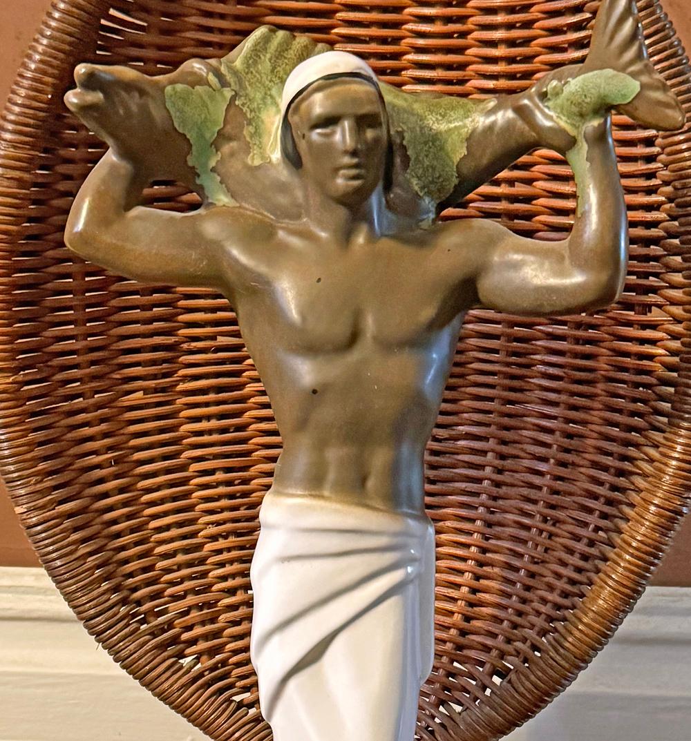 Estremamente rara, questa raffinata figura in ceramica di un uomo seminudo delle isole del Pacifico o delle Hawaii che tiene in equilibrio un grande pesce sulle spalle è splendidamente smaltata nei toni dell'avorio e del marrone noce moscata,