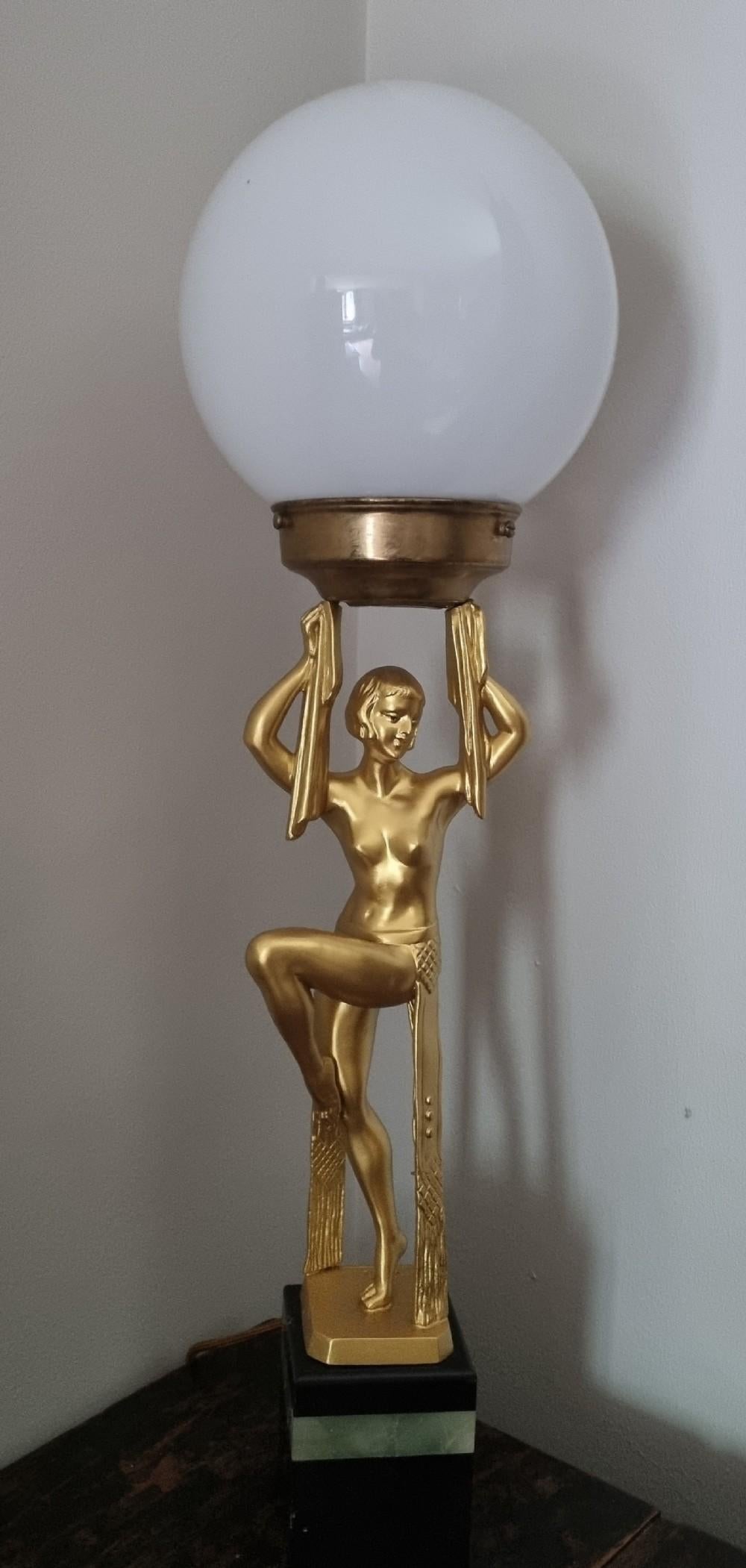 Lampada da tavolo francese Art Déco degli anni '30 con una figura dipinta in oro di una ballerina nuda in una posa stilizzata di ispirazione egiziana. Sostiene un paralume a globo in vetro con braccia drappeggiate, in piedi su una base a gradini in