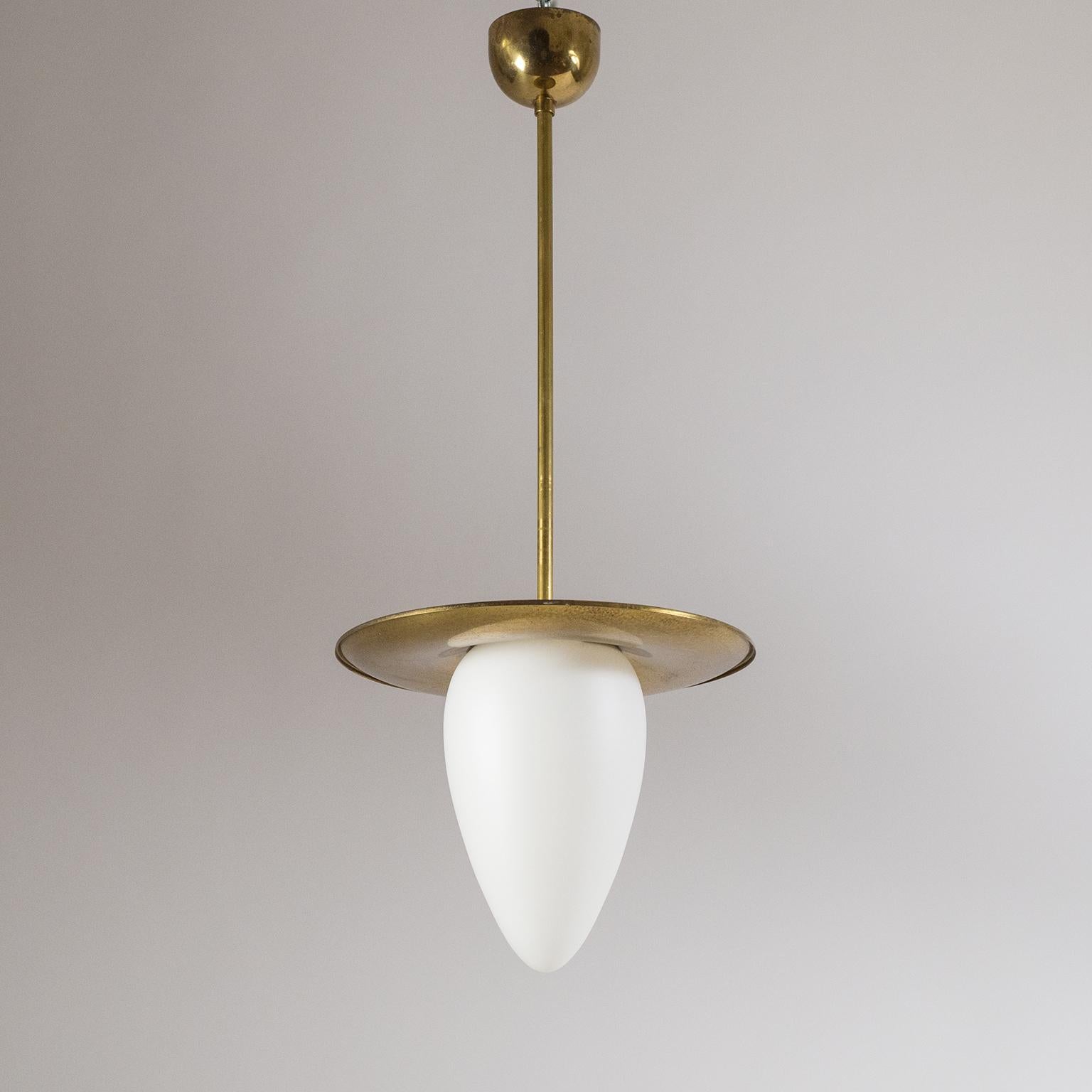 Very fine brass and satin glass pendant from the 1930s. An elongated glass diffuser with satin finish fits snugly underneath a curved brass shade. The Minimalist approach of this fixture already reflects the modernist ideas of post-war modernism.