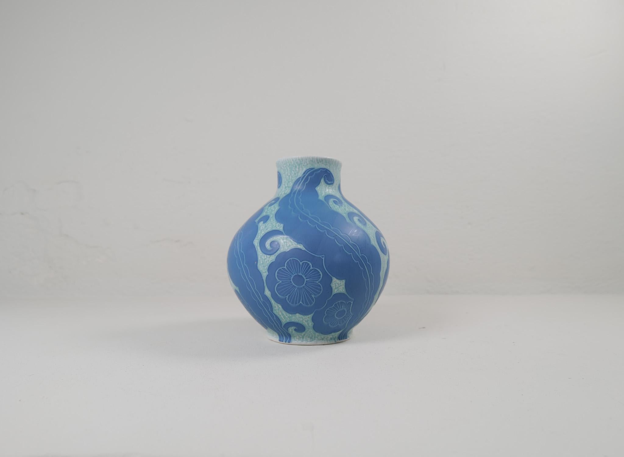 Sgraffito-Vase im Art déco-Stil mit Blumenmotiv, von Josef Ekberg für Gustavsberg.
Sgraffito ist eine Art, zwei Schichten zu einem Muster zu verbinden. Die zweite Schicht wird abgekratzt und übrig bleibt ein hellblauer Hintergrund mit einem schönen