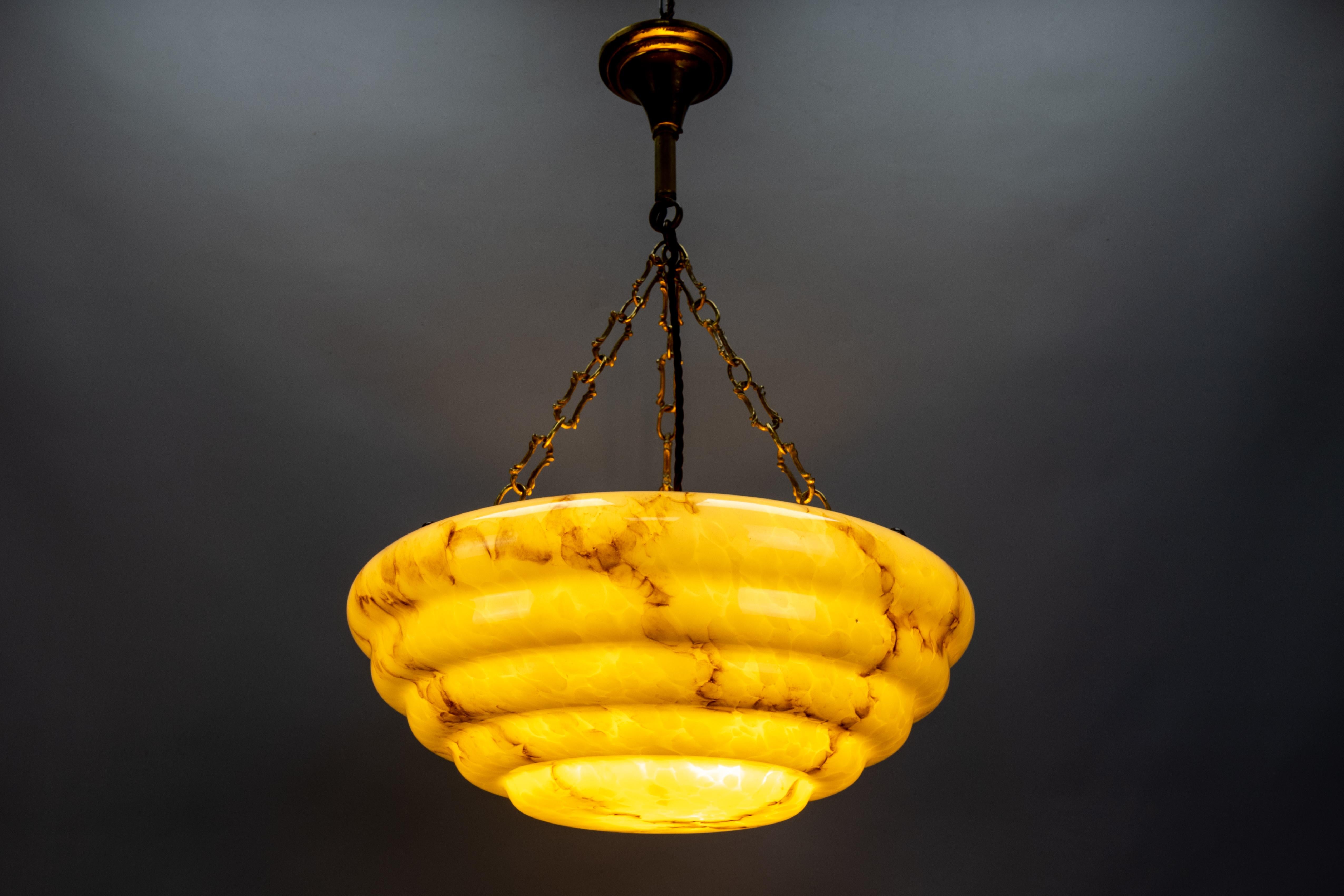 Una lampada a sospensione in stile Art Deco in vetro e ottone, in stile marmorizzato e stratificato, di colore beige giallastro e marrone, risalente agli anni '50, in Germania.
Questa bellissima plafoniera è caratterizzata da un paralume in vetro