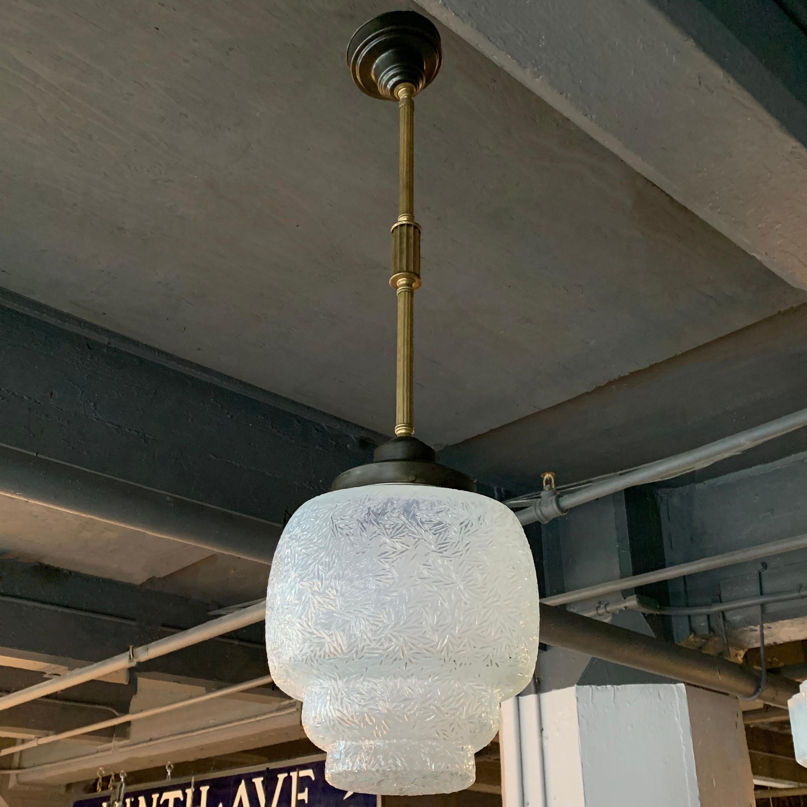 Cette suspension Art Déco est composée d'un abat-jour en verre opalin à motifs givrés sur un poteau décoratif en acier et en laiton avec un baldaquin. Le pendentif est nouvellement câblé pour accepter jusqu'à une ampoule à culot moyen de 200 watts.