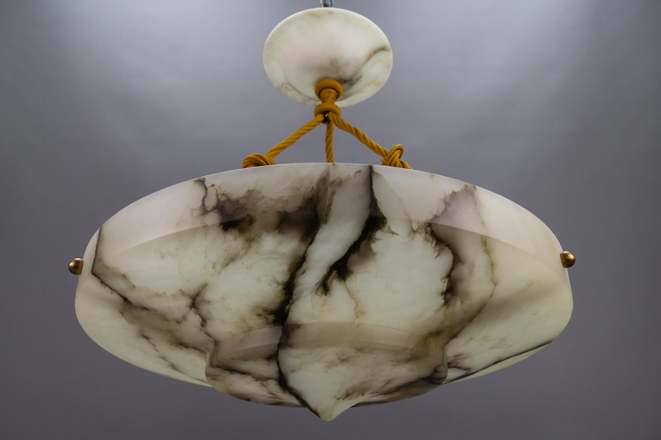 An elegant, round, layered Art Deco period ceiling pendant light featuring a lampshade - a bowl - of white alabaster with impressive black and dark brown veins. Germany, around 1920.
Masterfully carved in layered form, this beautifully veined