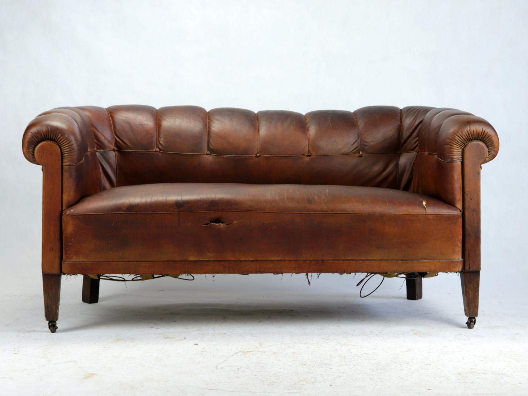 Antique Art Deco brown leather seating set consisting of two barrel club chairs and a sofa with great Aged Patina.
These stylish club chairs have a great shape due his shell back and have wheels at the front.

The frame is still firm and the seat