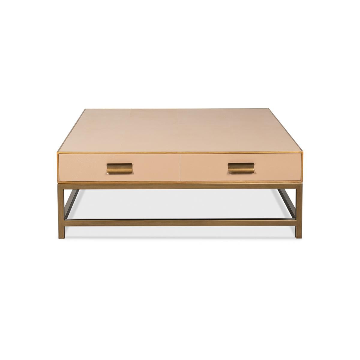 Crafted from wood with a shagreen embossed leather wrapped top, this square coffee table is finished with gold trim and hardware. With two drawers and raised on cube-form base with stretchers. 
The low-profile design makes it ideal for a functional